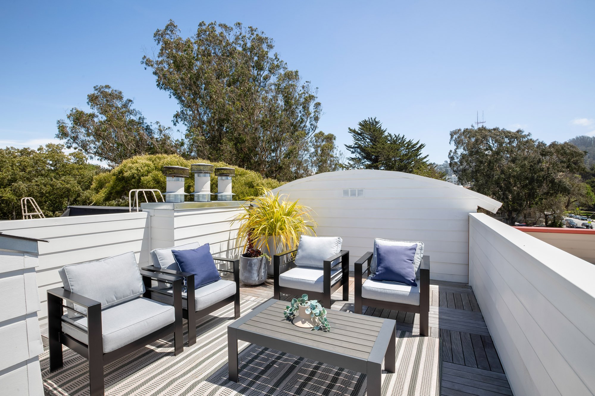 Private deeded ooftop deck at 2172 Fell Street San Francisco with outdoor lounge seating, navy accent pillows, composite wood decking, potted plants, and panoramic views of Panhandle treetops and Sutro Tower
