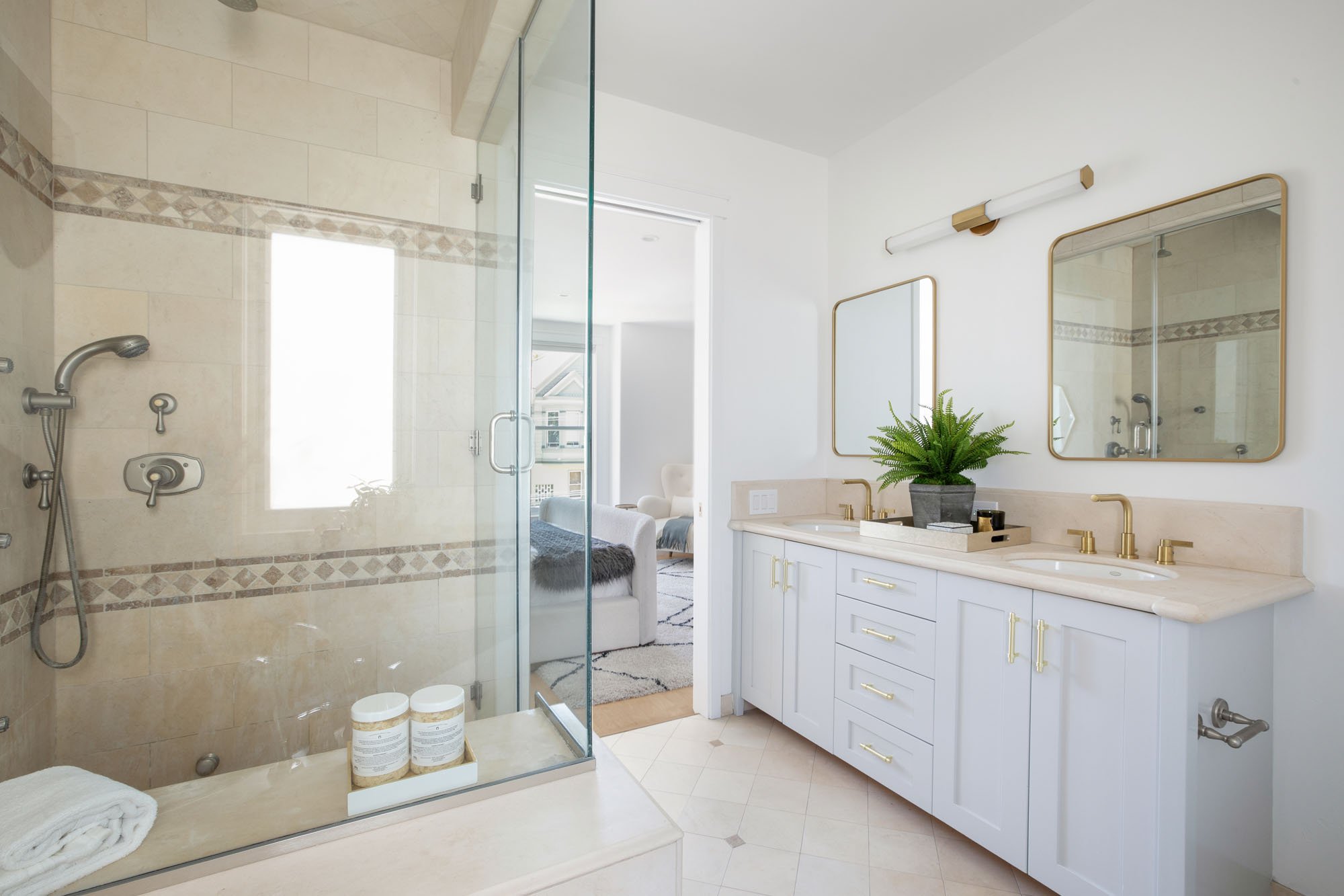 High-end bathroom design showcasing a white shaker-style double vanity, satin gold faucets, and a stone tile walk-in shower with a rainfall showerhead.