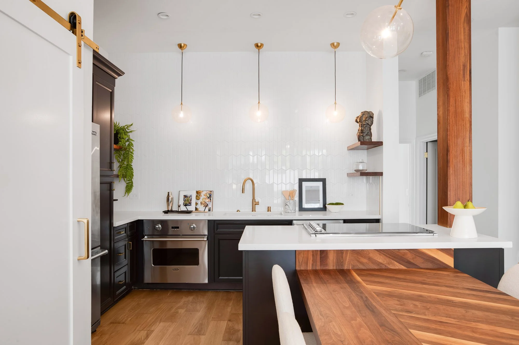 Designer kitchen in 4545 18th Street San Francisco TIC with black Shaker cabinets, white quartz countertops, white chevron zellige tile backsplash, Viking stainless steel oven, brass pendant lights, gold gooseneck faucet, and walnut beam accent