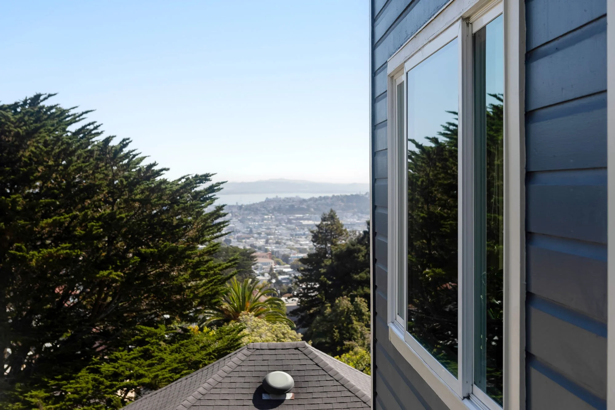 Close-up of the blue wood siding and window of 144 Lower Terrace, showcasing the panoramic view of the San Francisco Bay and city skyline in the distance.