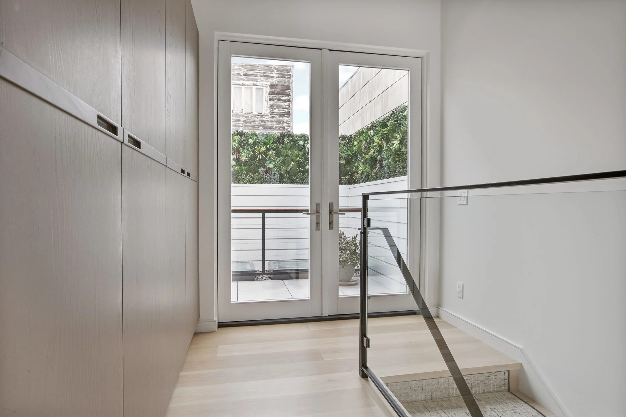 Modern upper-level landing at 290 Day St with custom millwork closets and glass doors leading to a private terrace with a vertical garden.