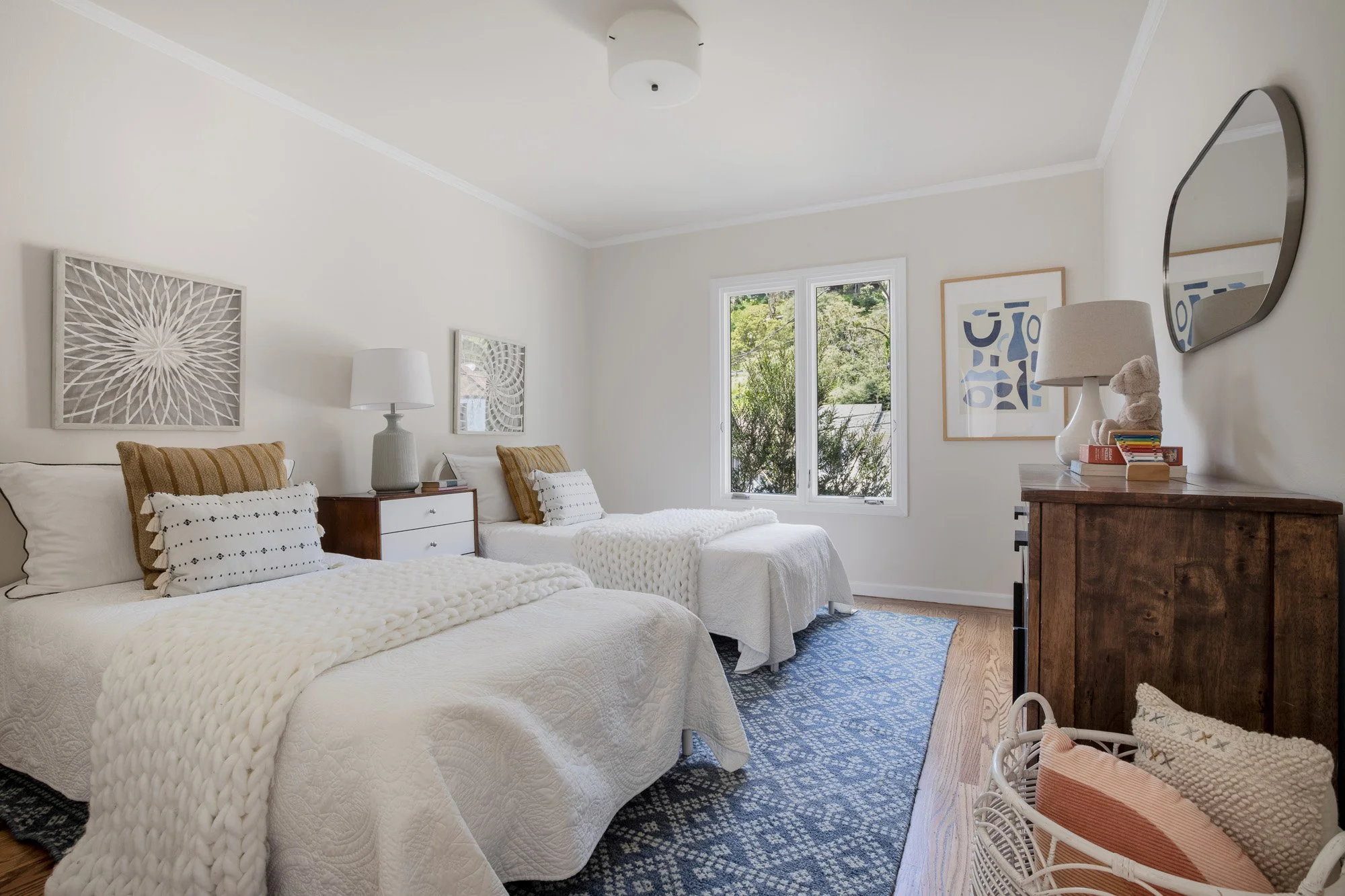 Family-friendly bedroom featuring twin beds with white textured linens, blue patterned rug, and mid-century modern furniture.
