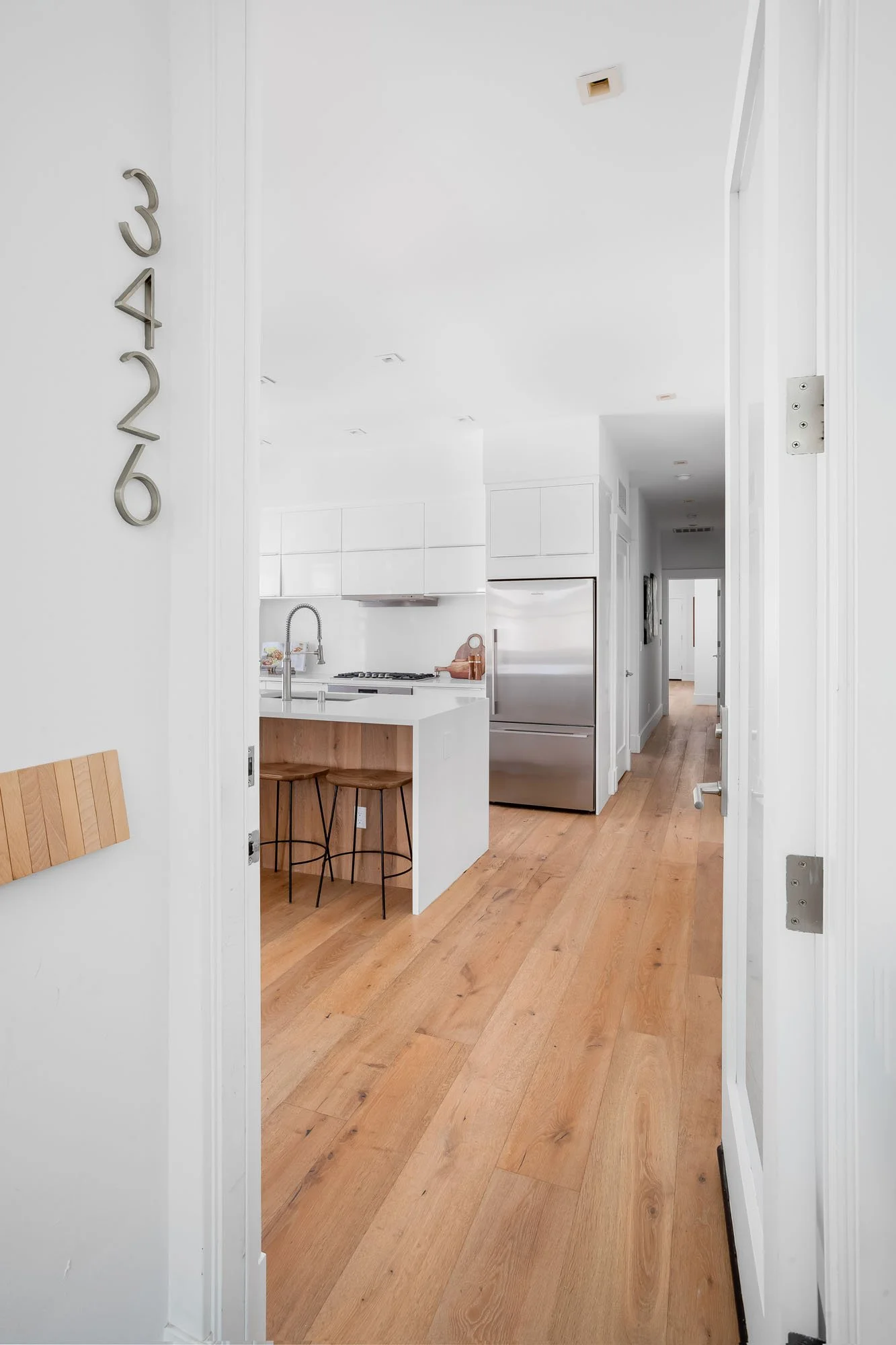 Bright interior entryway of 3426 19th St showing light hardwood floors and a modern white kitchen with stainless steel appliances.