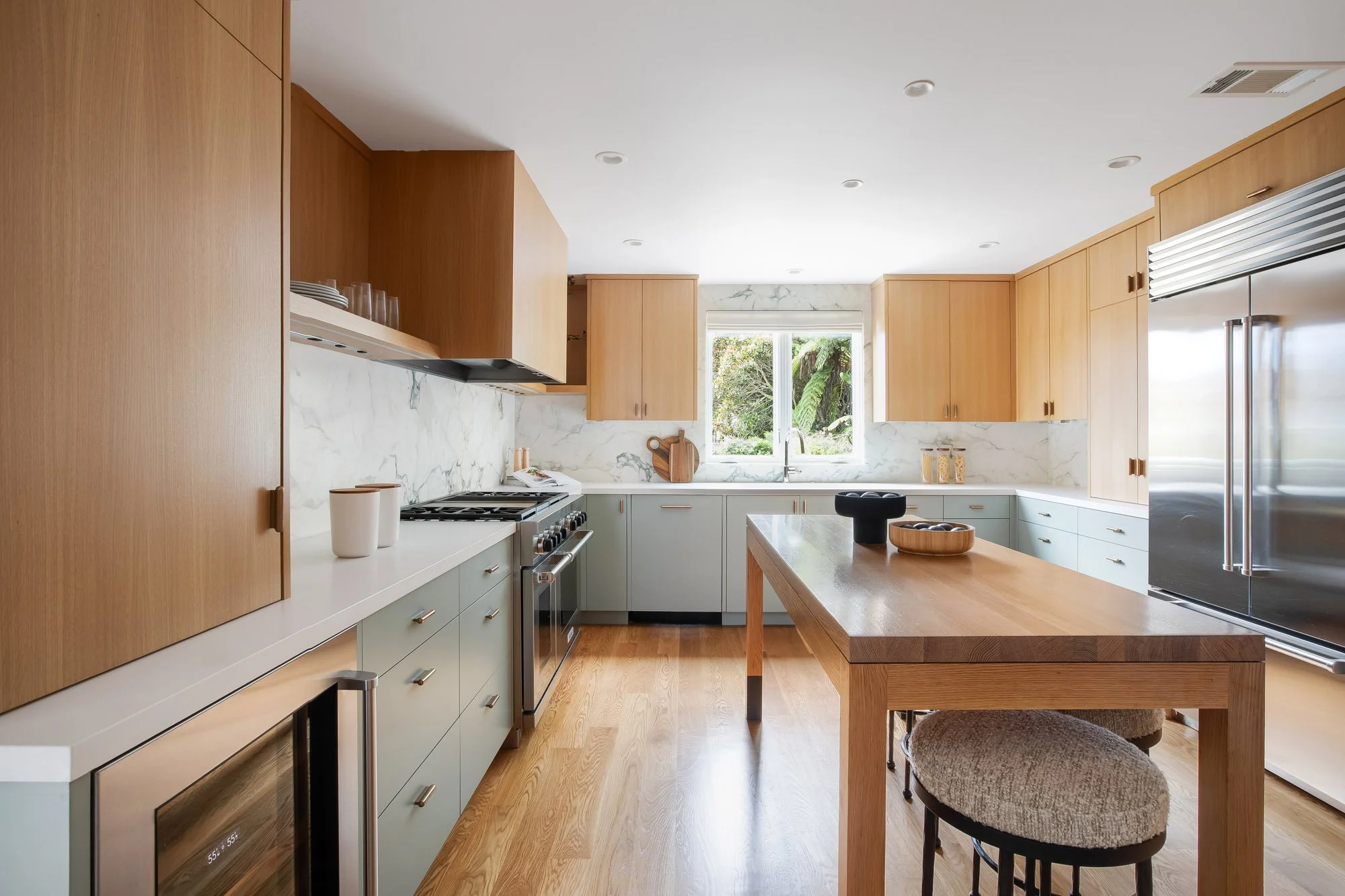Open kitchen at 771 Elizabeth Street in Noe Valley showing a Sub-Zero refrigerator, integrated wine cooler, custom counter-height oak island with seating, garden window, and white oak hardwood floors