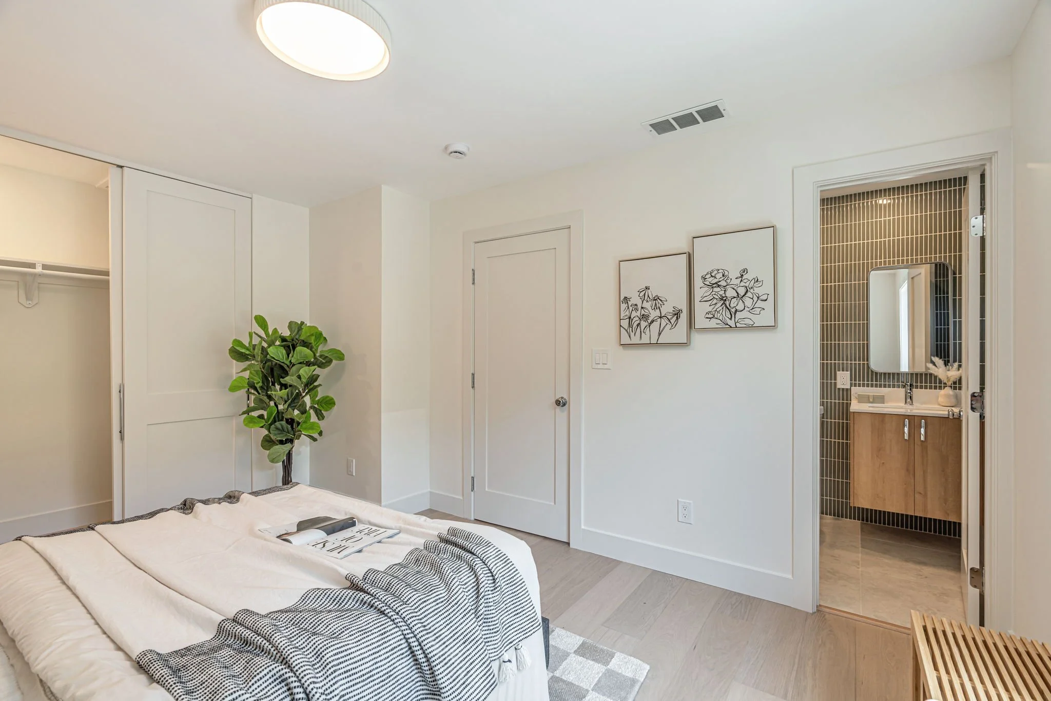 A view of the primary bedroom layout showing the white entry door, a sliding closet door, and the entrance to the ensuite bathroom. The bathroom features a modern floating wood vanity and a dark green, vertically tiled accent wall.