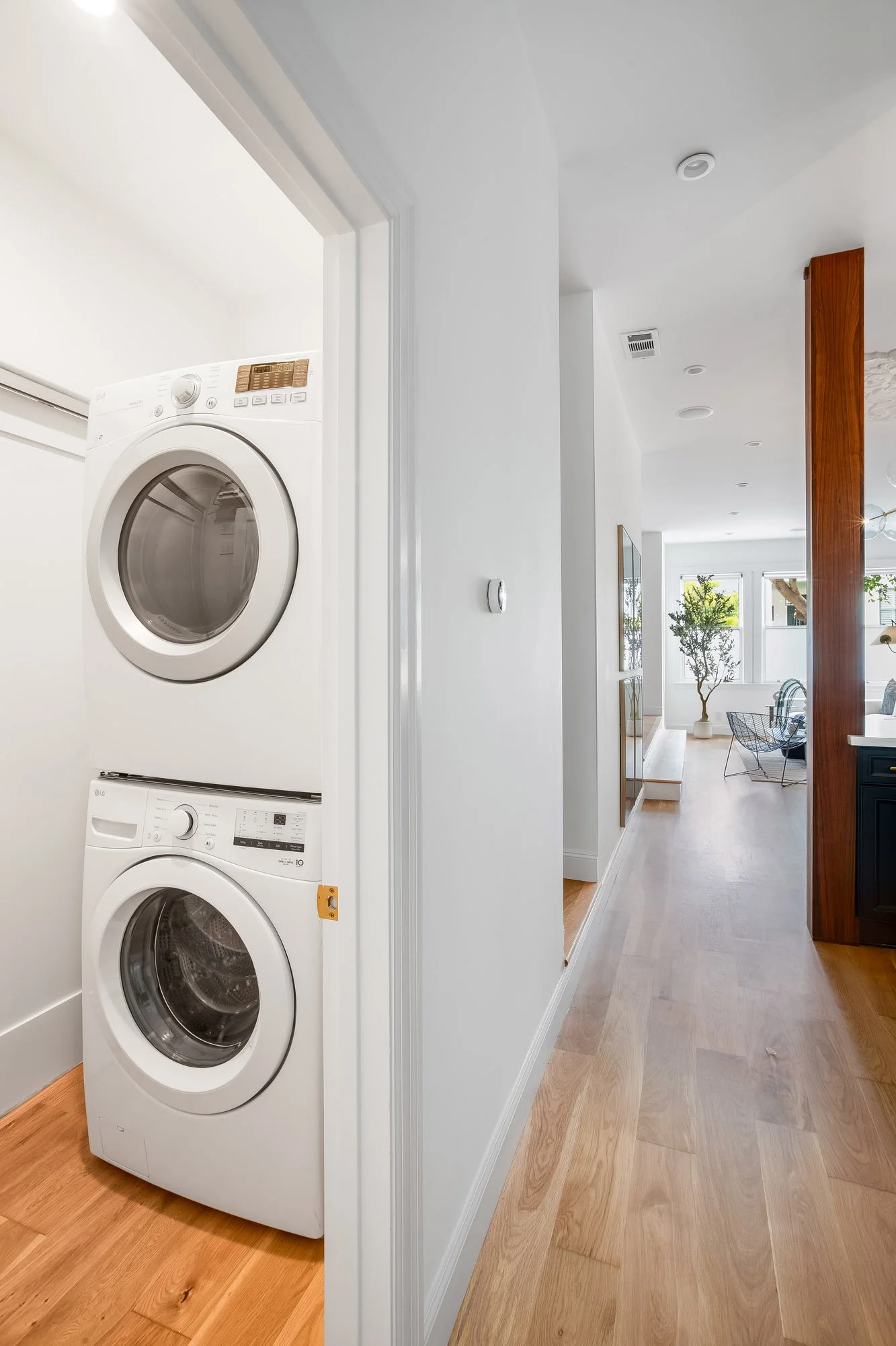 In-unit stacked LG washer and dryer in dedicated laundry alcove with white oak hardwood floors, opening to bright hallway with views to living room at 4545 18th Street Castro San Francisco TIC