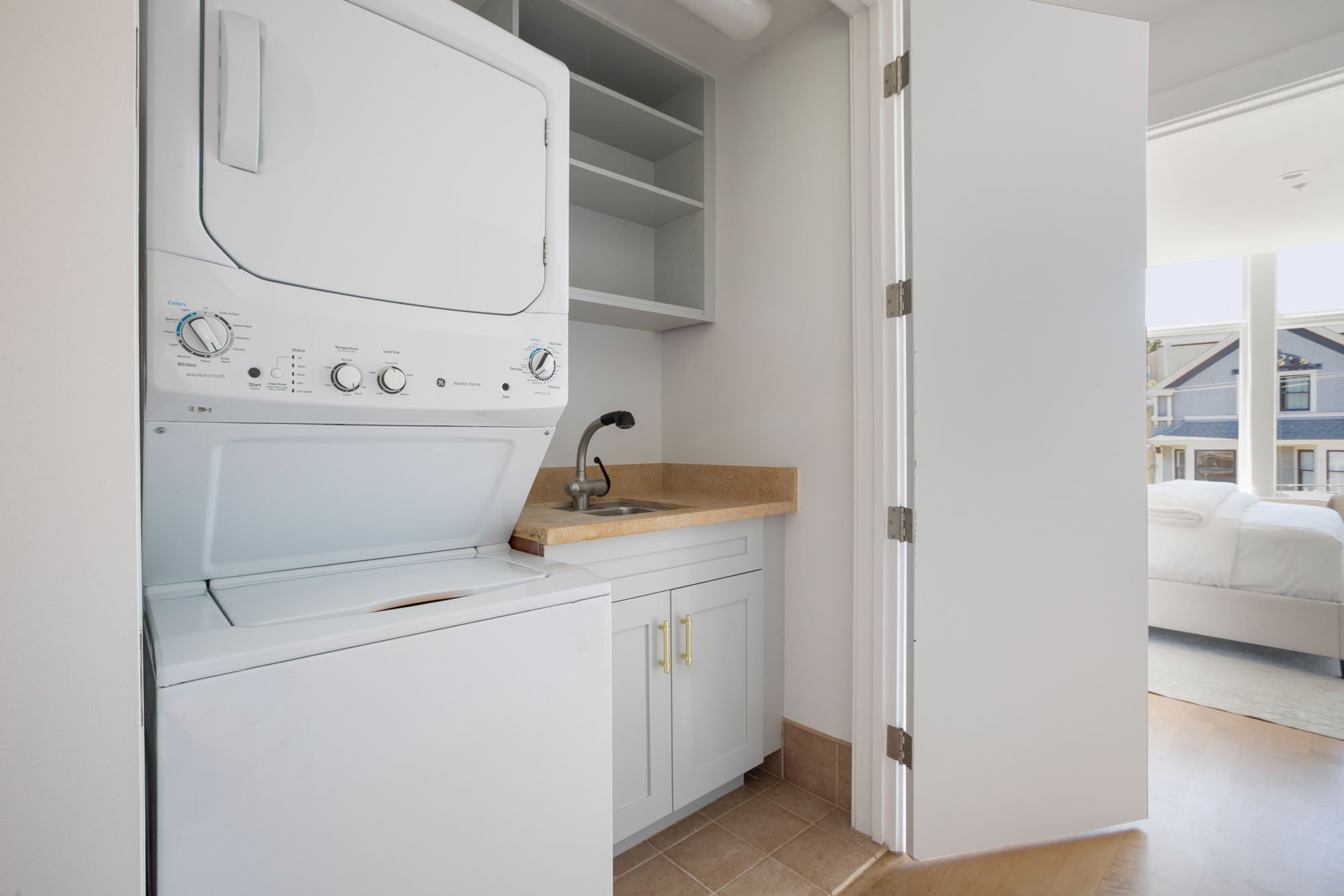Functional laundry closet design featuring a stacked washer and dryer unit, a small utility sink with a stone countertop, and built-in storage shelving.