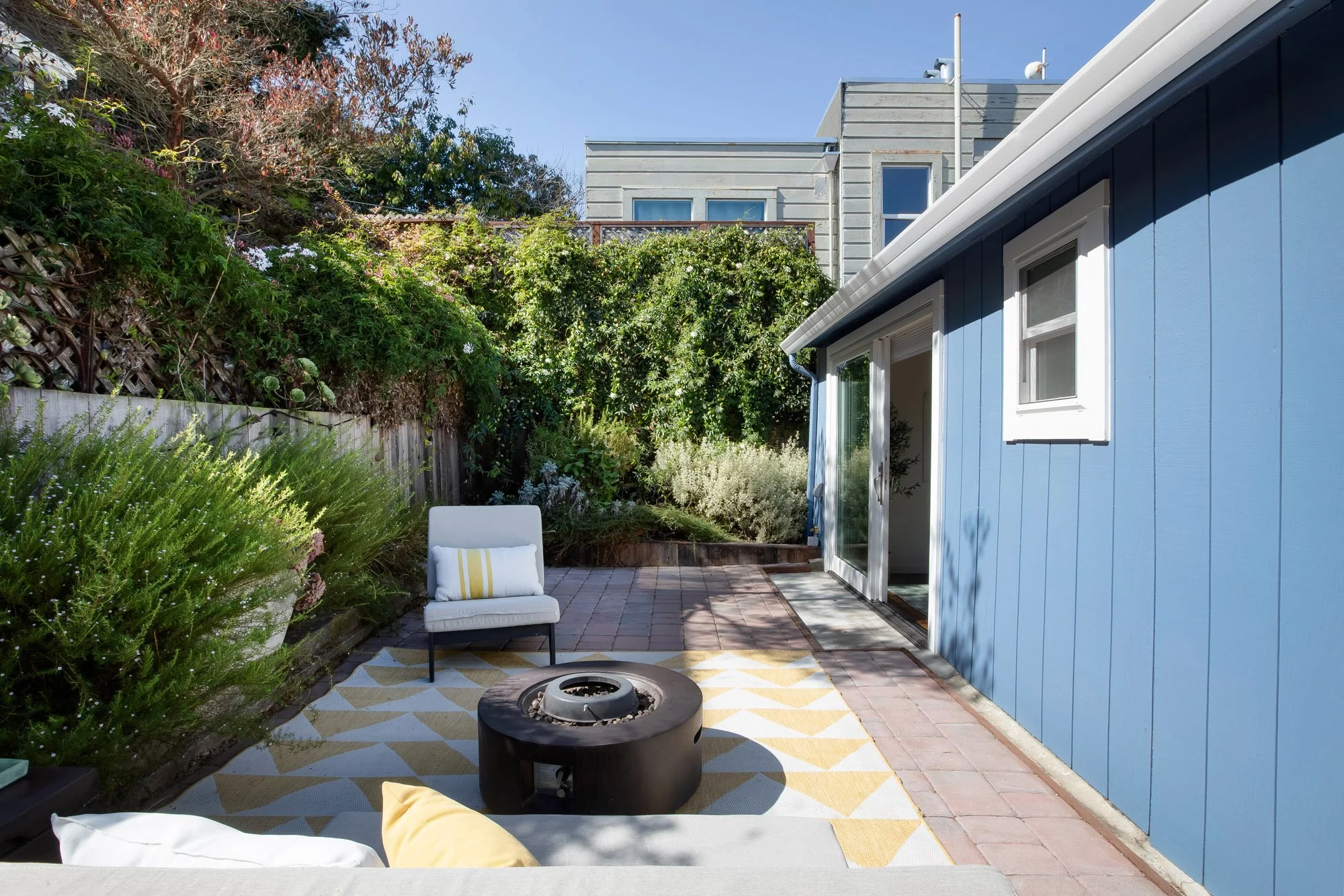 South-facing rear garden at 465 30th Street with a pavered patio, terraced drought-tolerant plantings and a sliding door into the second living area