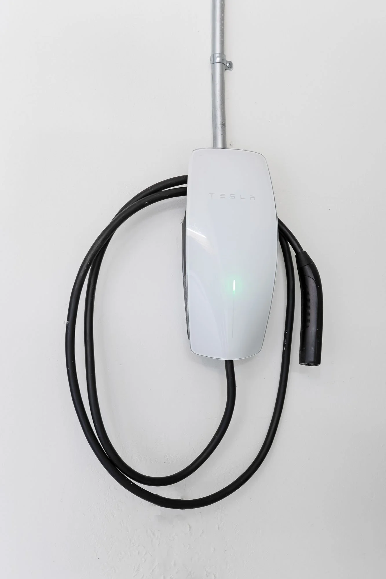A white Tesla Wall Connector electric vehicle (EV) charger professionally installed on a white garage wall.