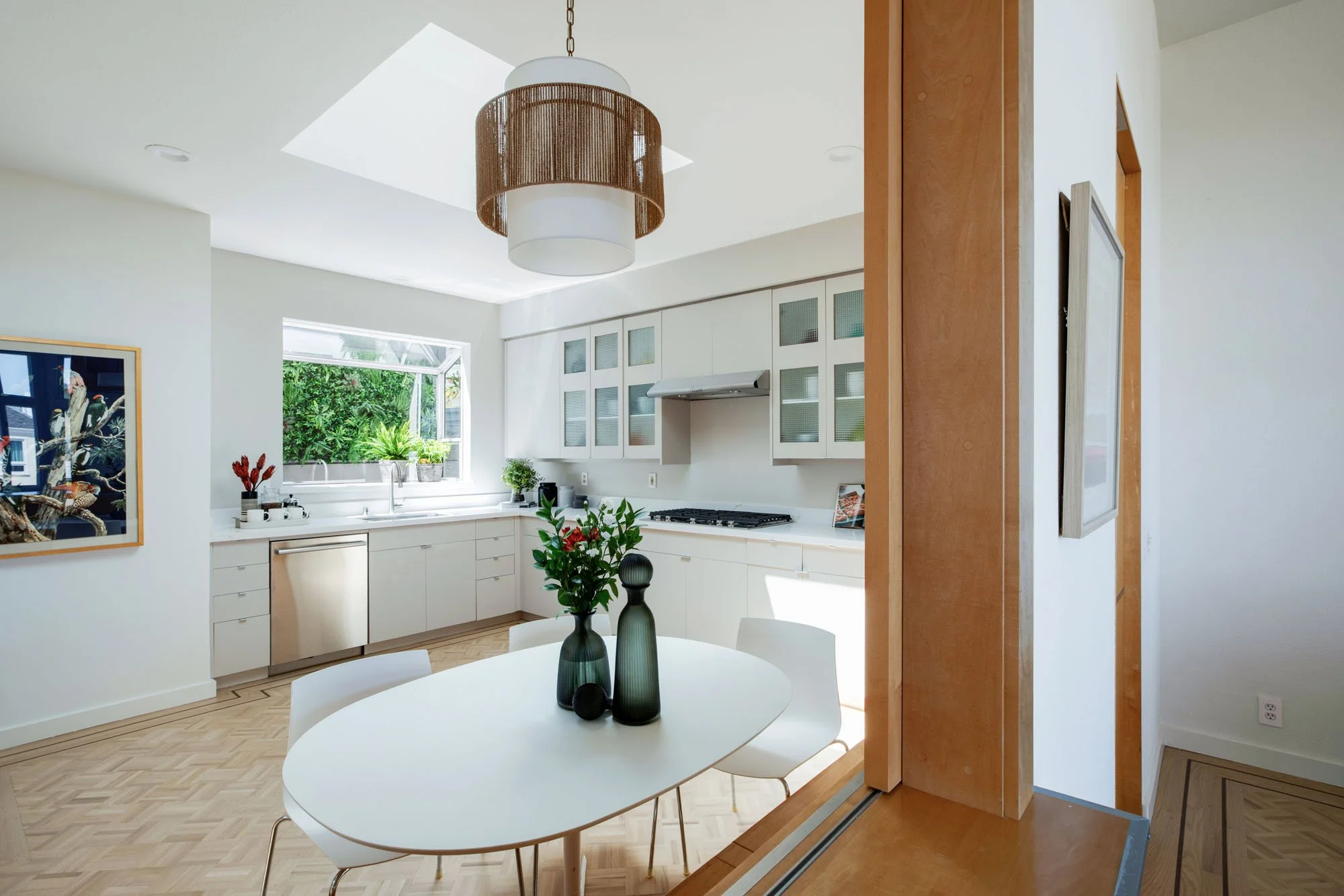 Bright open-concept kitchen and dining area with a modern rope-textured pendant light, integrated stainless steel appliances, and a garden-view window.