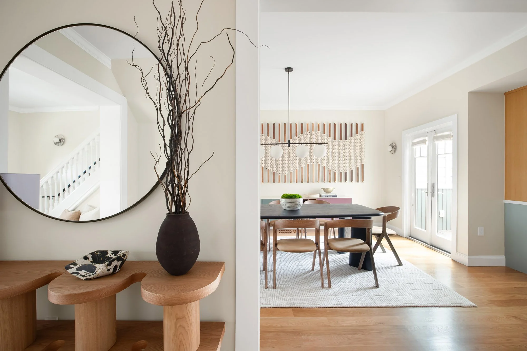 Entry foyer and dining room at 771 Elizabeth Street, framed by a round mirror and sculptural oak console, with a Windy Chien "Hitching Post" cordage installation and French doors beyond.