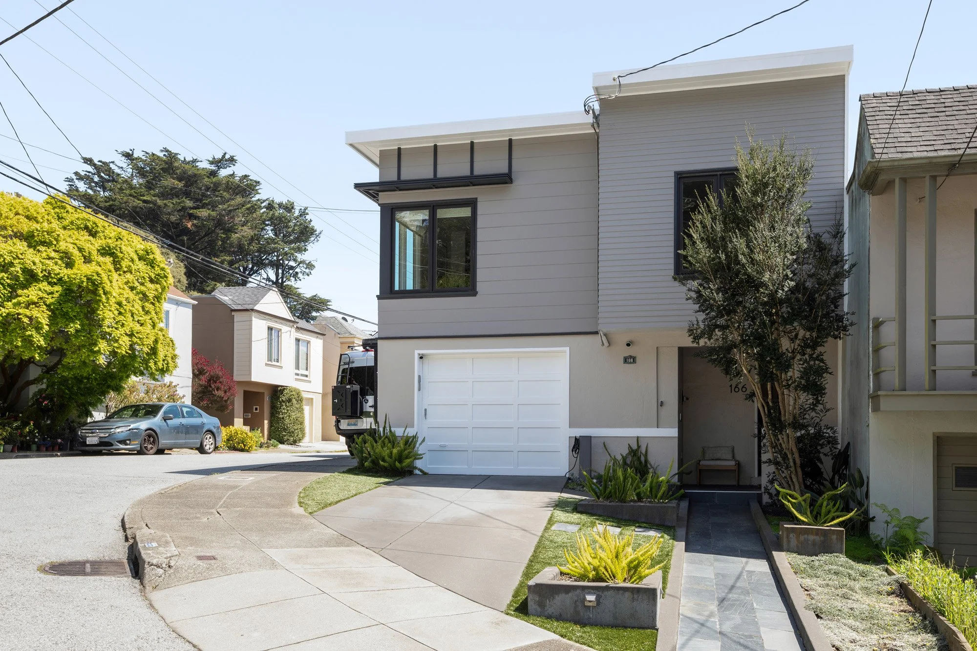 Contemporary two-story home exterior with a white garage door, neutral gray siding, and a clean, modern architectural silhouette.