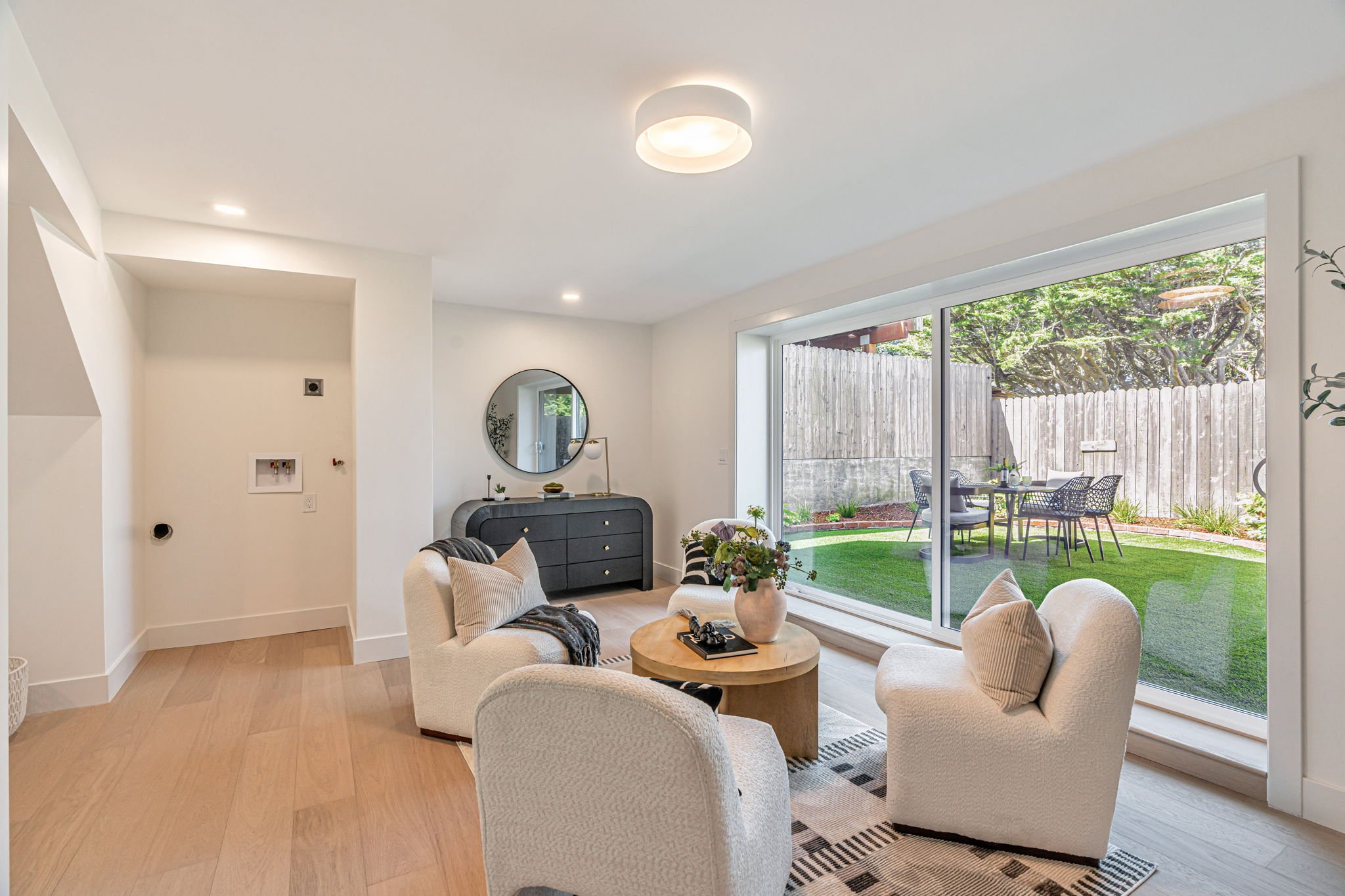 Interior view of a luxury lounge room in San Francisco, showing a black mid-century modern sideboard with a round mirror and large sliding glass doors that provide views of the private backyard.