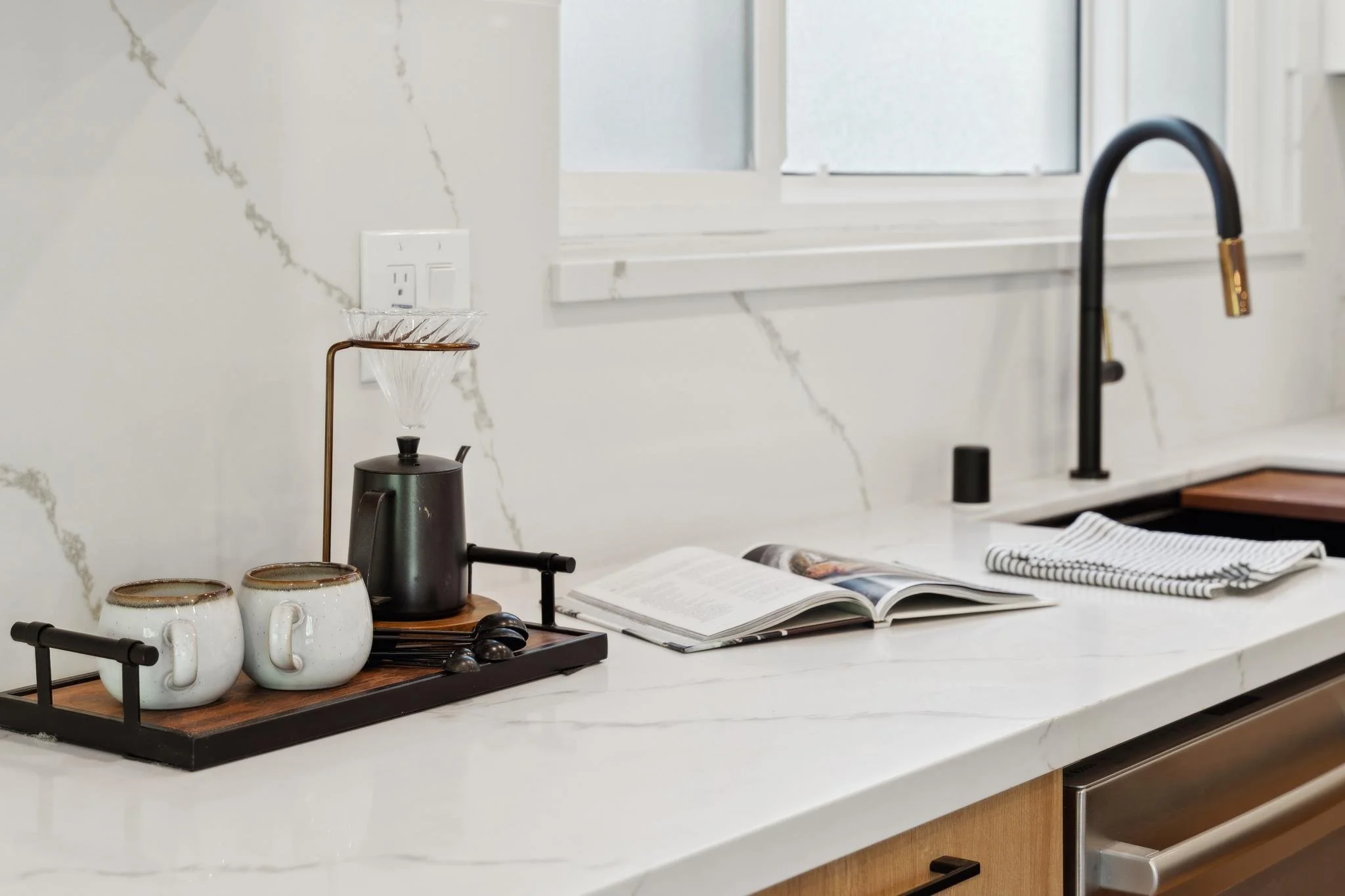 Close-up of a designer coffee station on a white marble countertop with a pour-over dripper, matte black kettle, and luxury kitchen accessories.