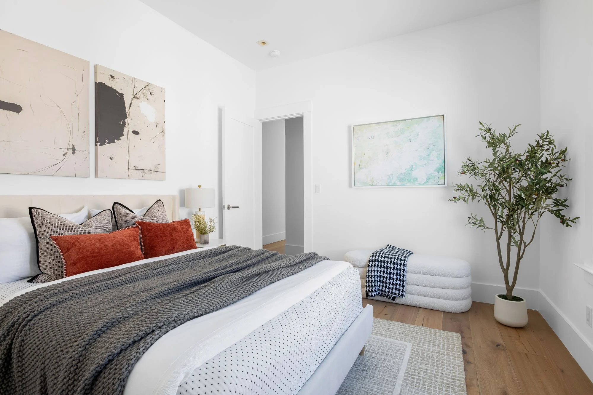 Minimalist bedroom design in Mission Dolores with an indoor olive tree, abstract wall art, and a white bouclé storage bench.