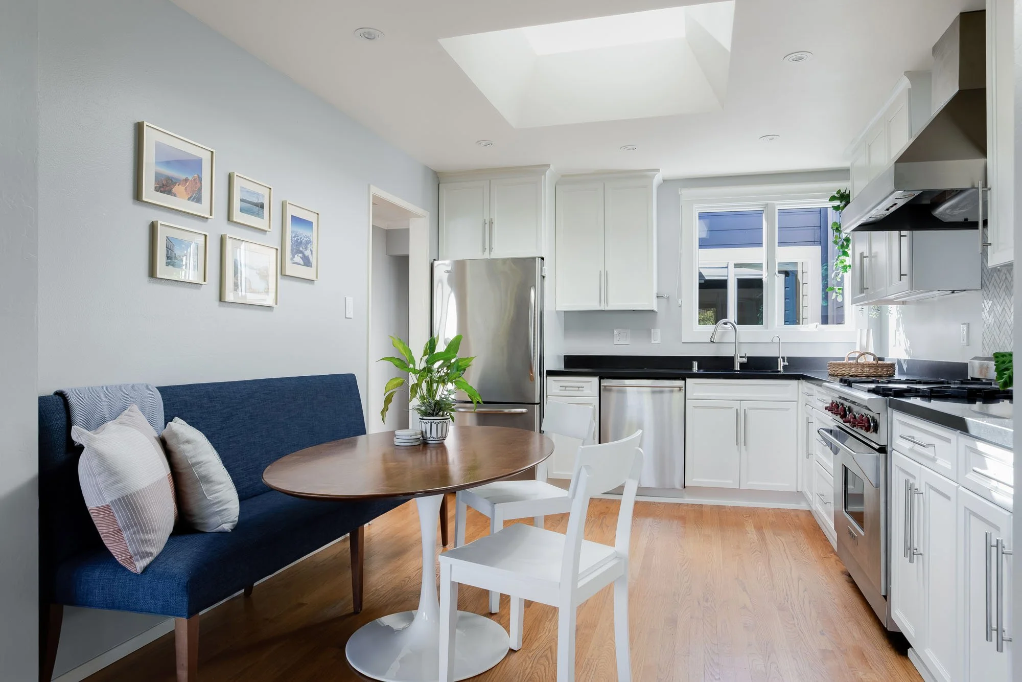 Cozy breakfast nook in the kitchen featuring a blue upholstered bench, a tulip-style pedestal table, and a skylight providing natural light.