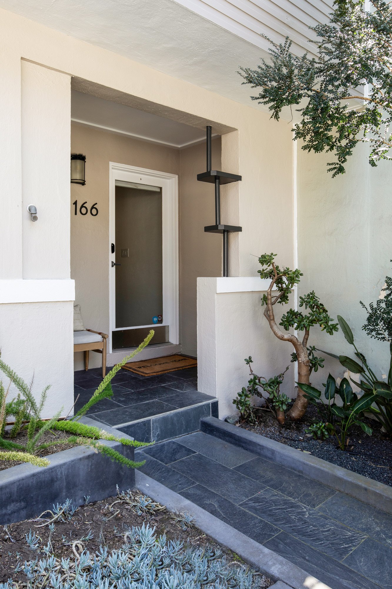 Modern front entryway featuring a slate tile path, minimalist address numbering, and professional drought-tolerant landscaping.