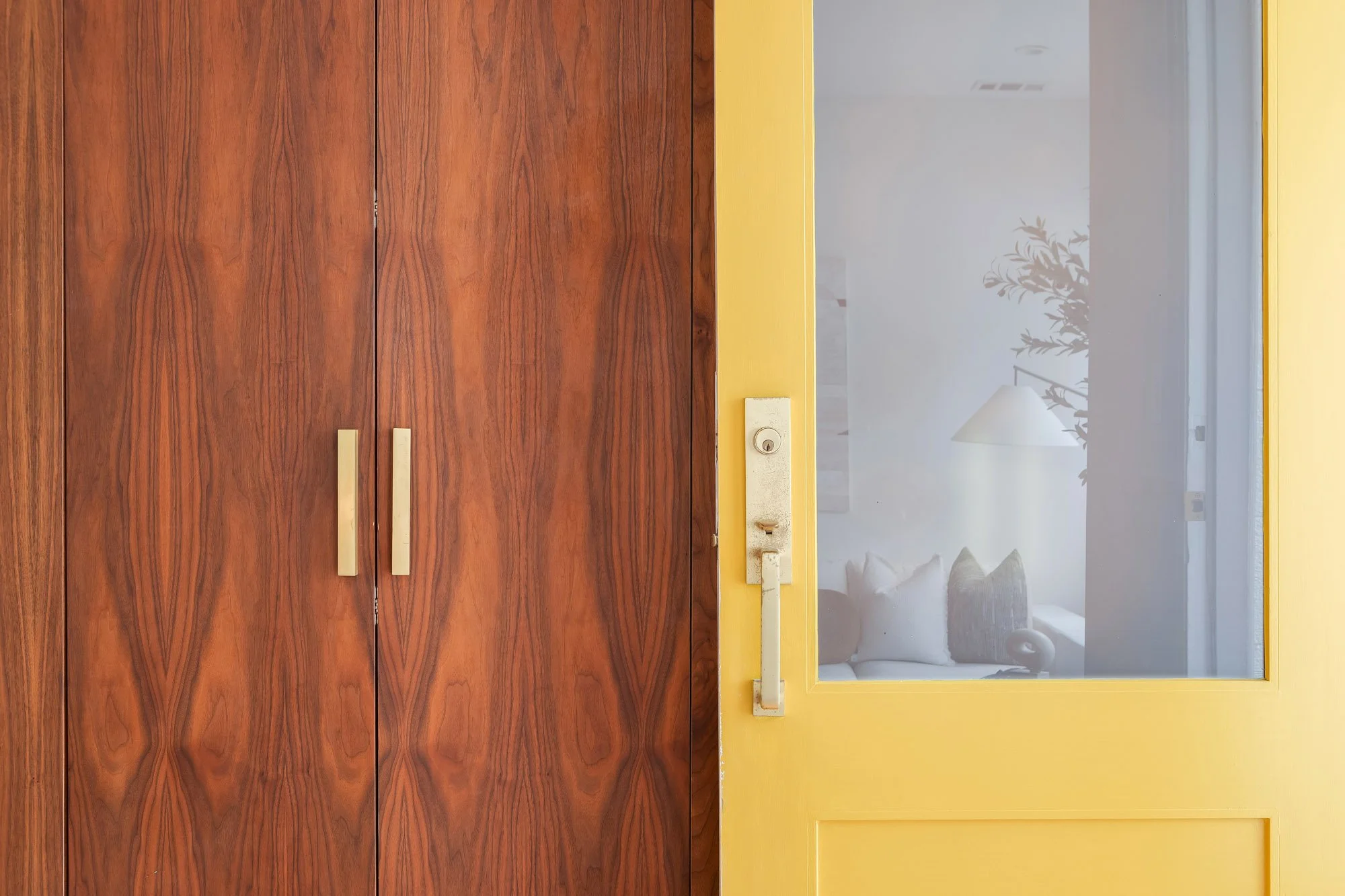 Close-up of bookmatched walnut built-in cabinet doors with brass bar pulls alongside bold yellow interior door with frosted glass panel and cast brass hardware in 4545 18th Street San Francisco luxury TIC