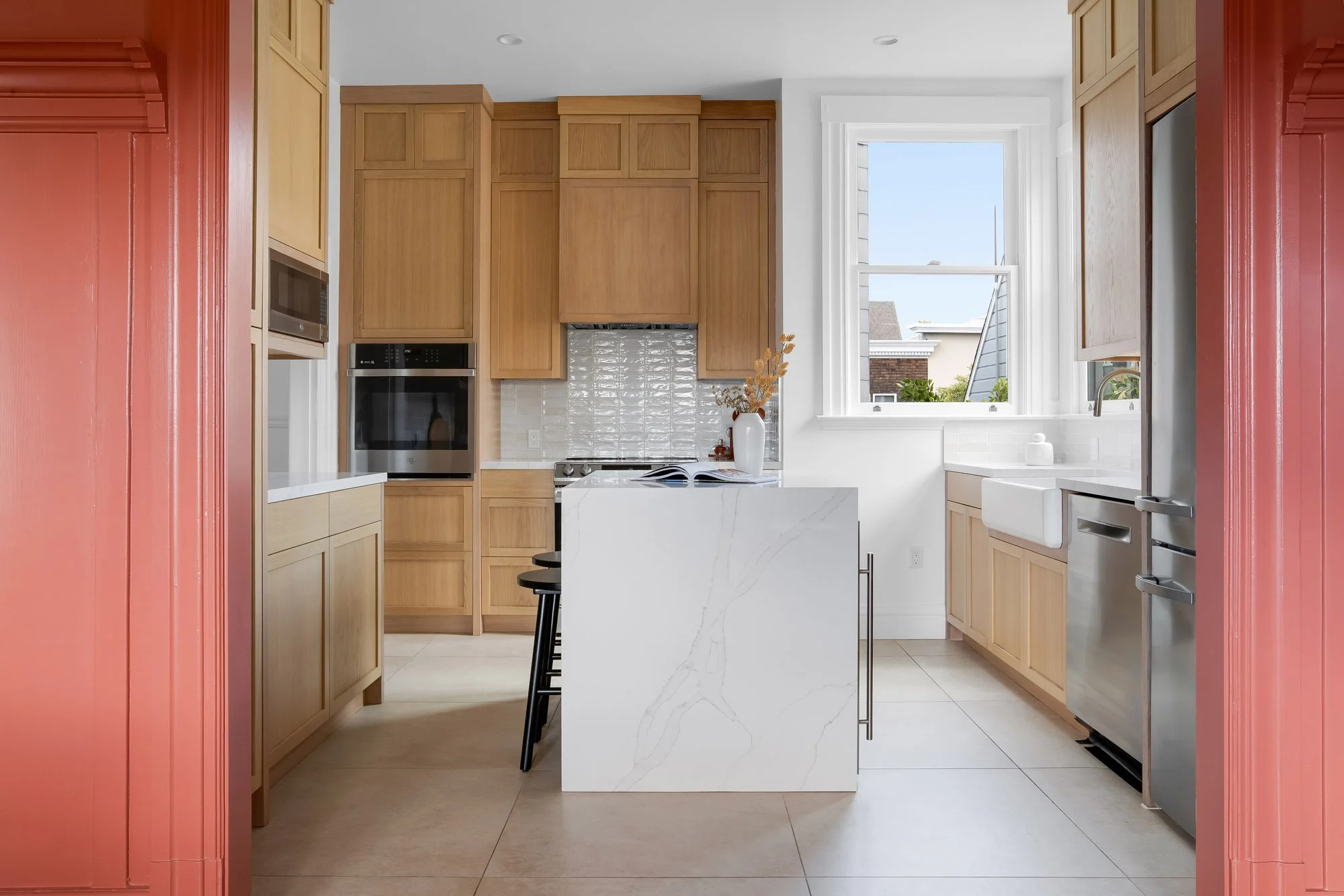 Custom white oak kitchen cabinetry with textured tile backsplash, marble waterfall island, farmhouse sink, and stainless steel appliances viewed through original Victorian doorway, Presidio Heights, San Francisco