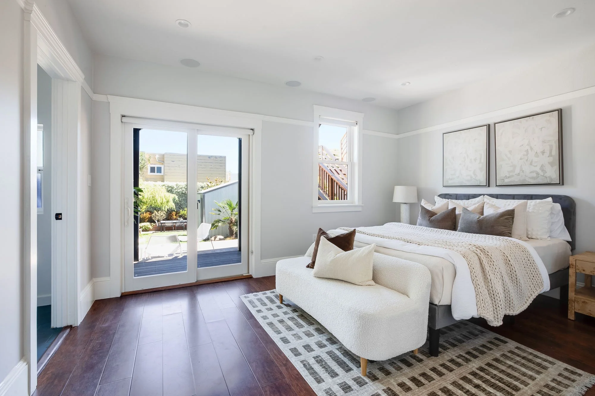 The primary bedroom at 246 Detroit featuring dark wood floors, a king-sized bed with textured linens, and sliding glass doors that open directly onto the backyard patio.