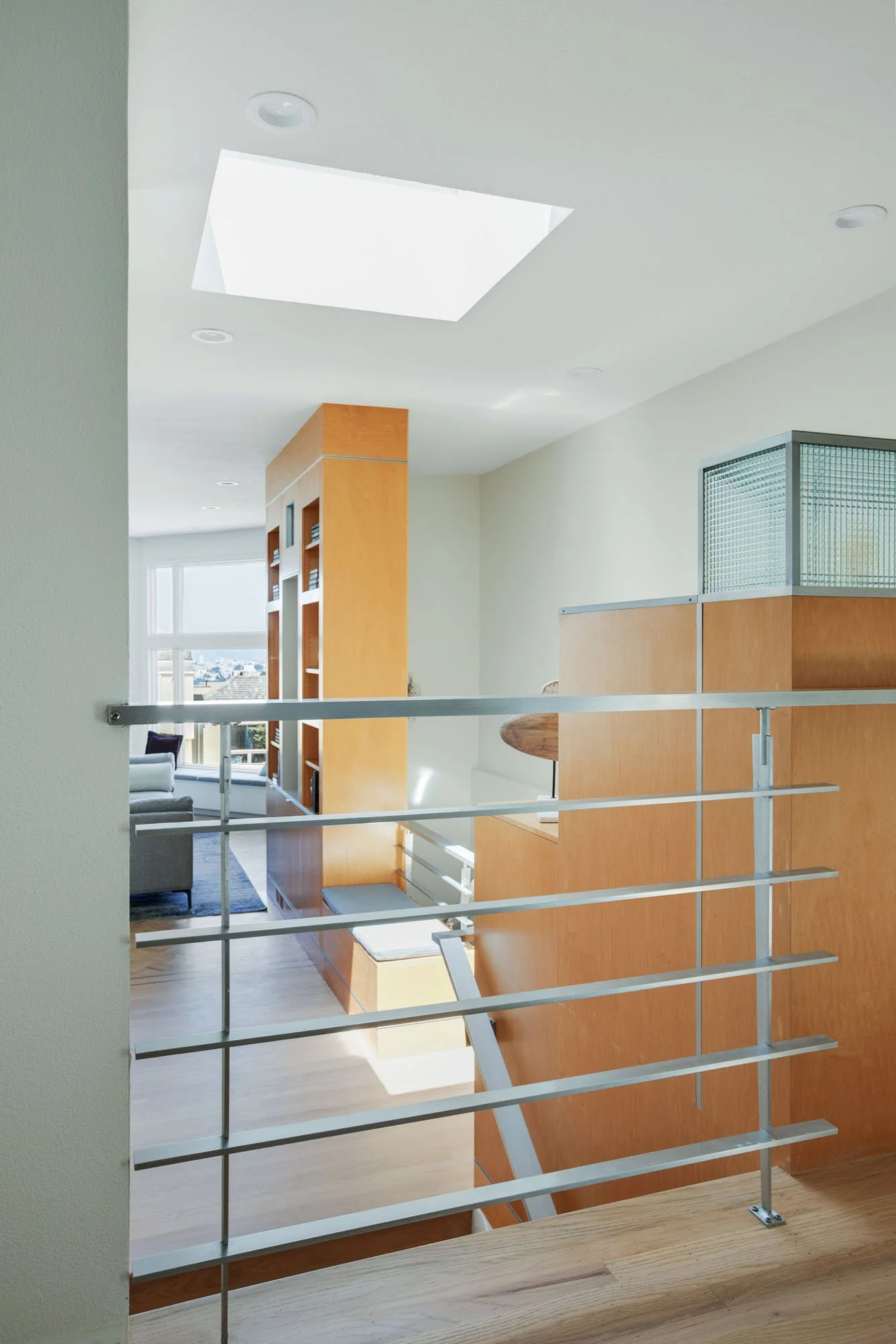 Modern interior view of a San Francisco home featuring a sleek metal balcony railing, custom wood built-ins, and a large skylight that floods the living space with natural light.