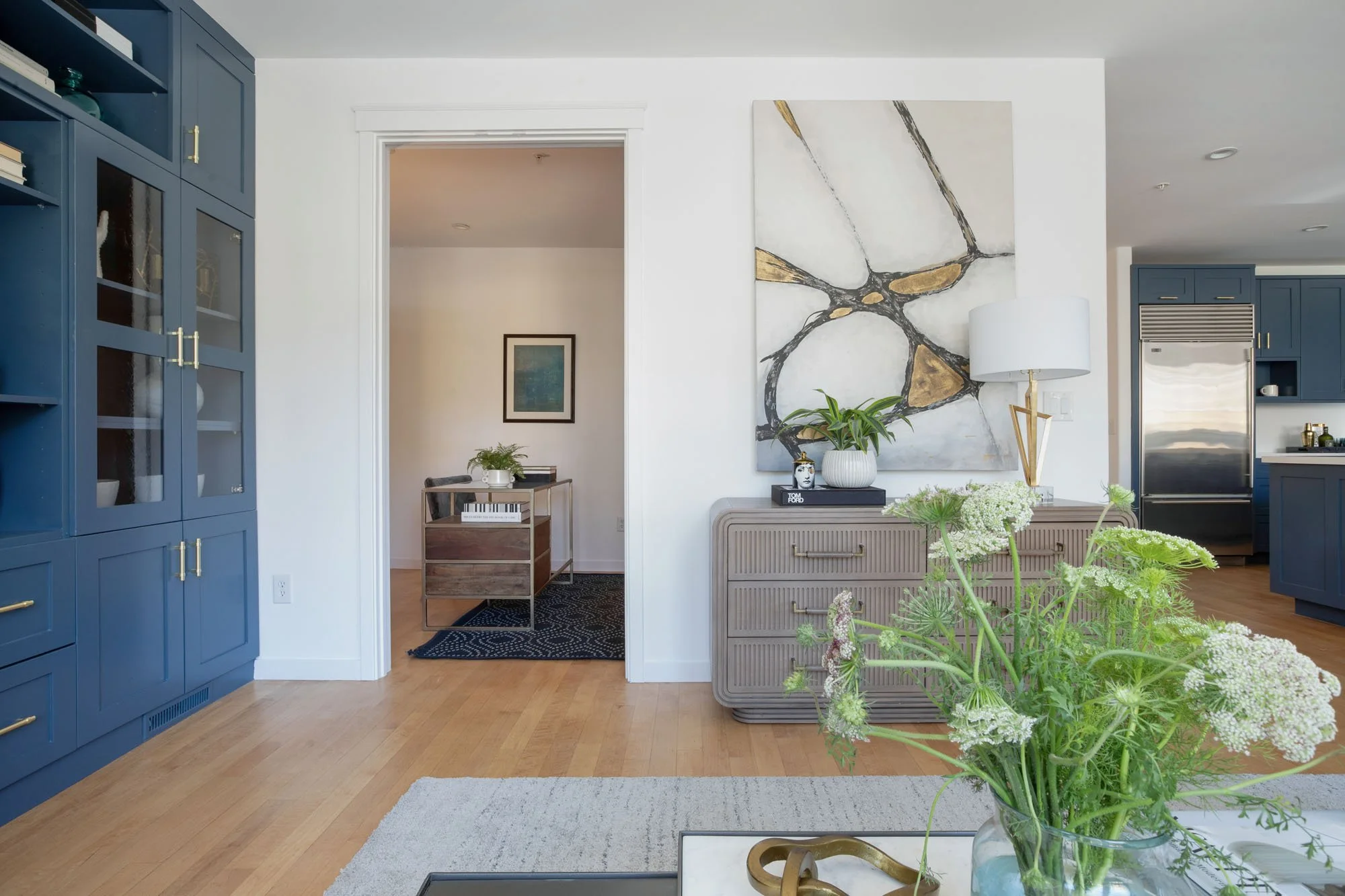 Modern interior design showcasing a transition from a slate blue built-in bookcase to a home office with a wood executive desk and geometric area rug.