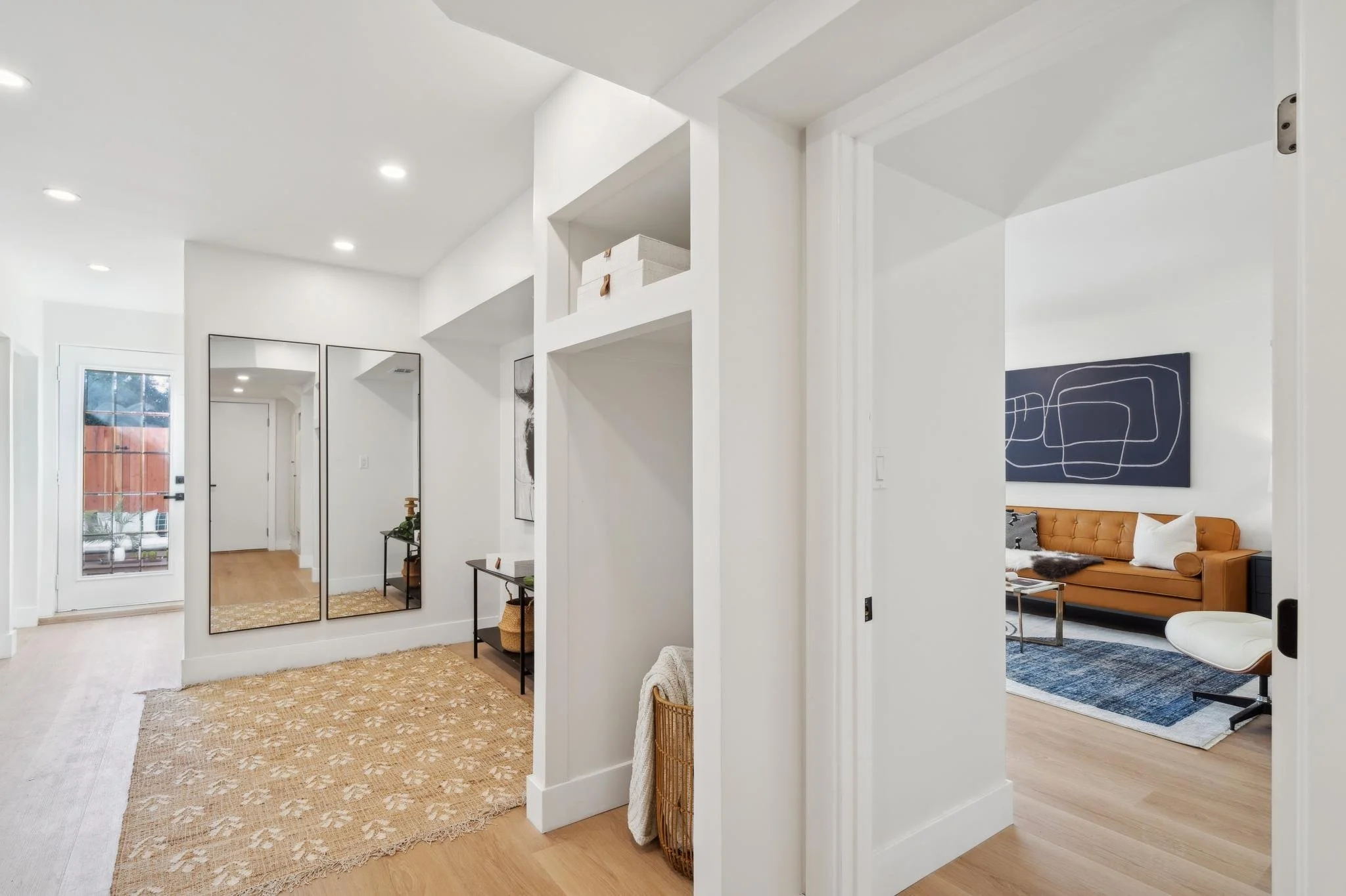 Functional entryway or lower-level landing showing a glimpse into a secondary living area with a tan leather sofa and mid-century modern furniture.