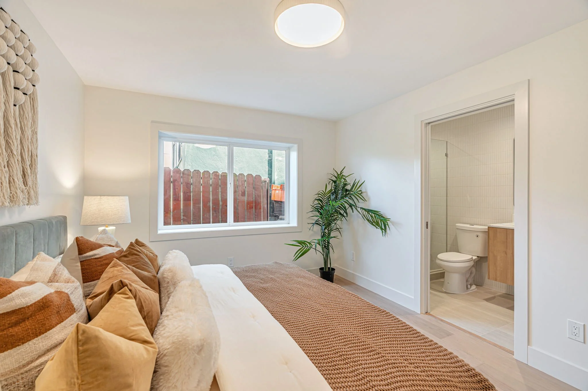 Sunny guest bedroom with an open ensuite bathroom, featuring a large horizontal window and light oak hardwood floors common in San Francisco luxury renovations.