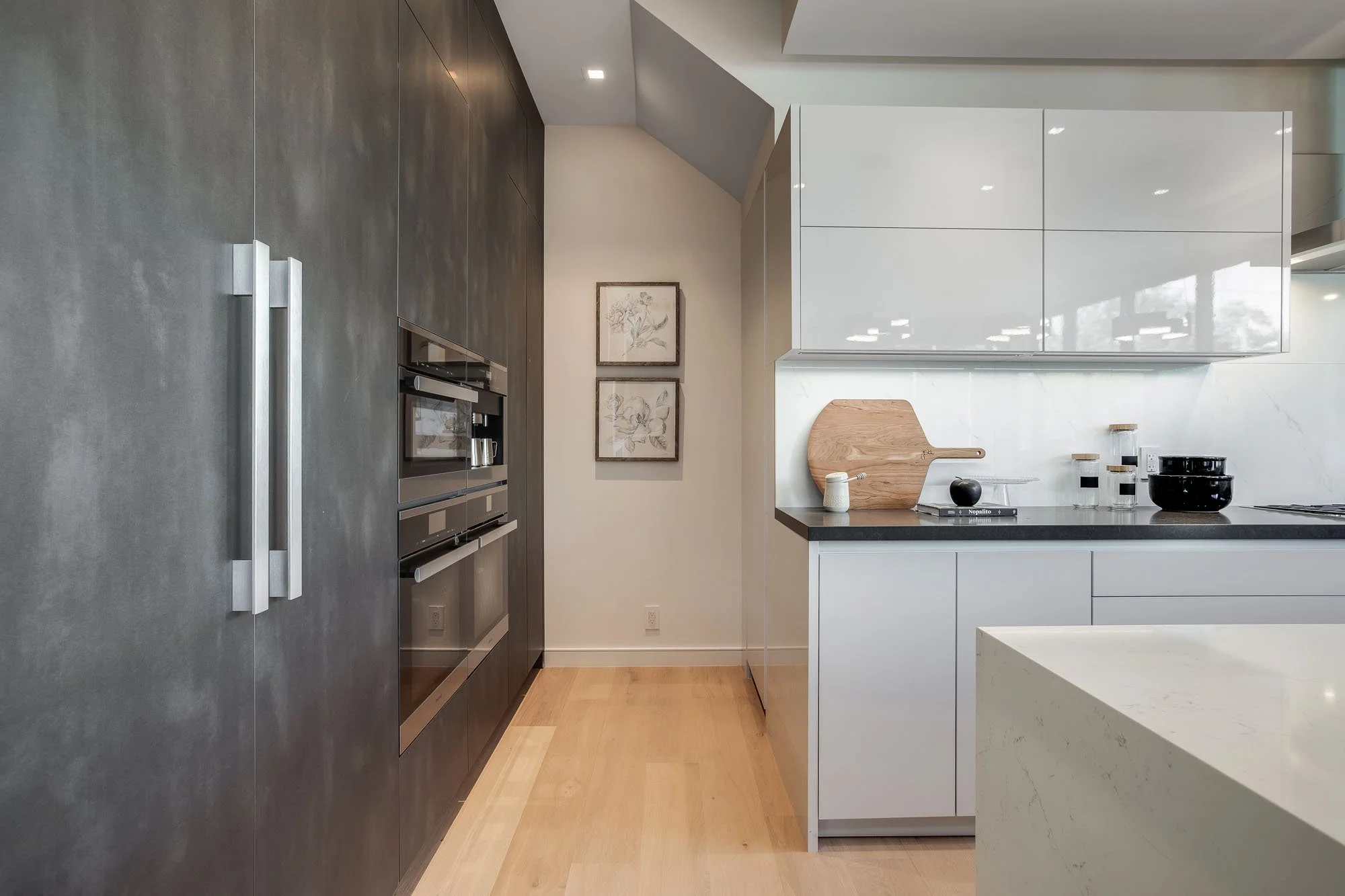 Minimalist gourmet kitchen detail featuring high-gloss white upper cabinets, integrated wall ovens, and a custom charcoal gray refrigerator wall.