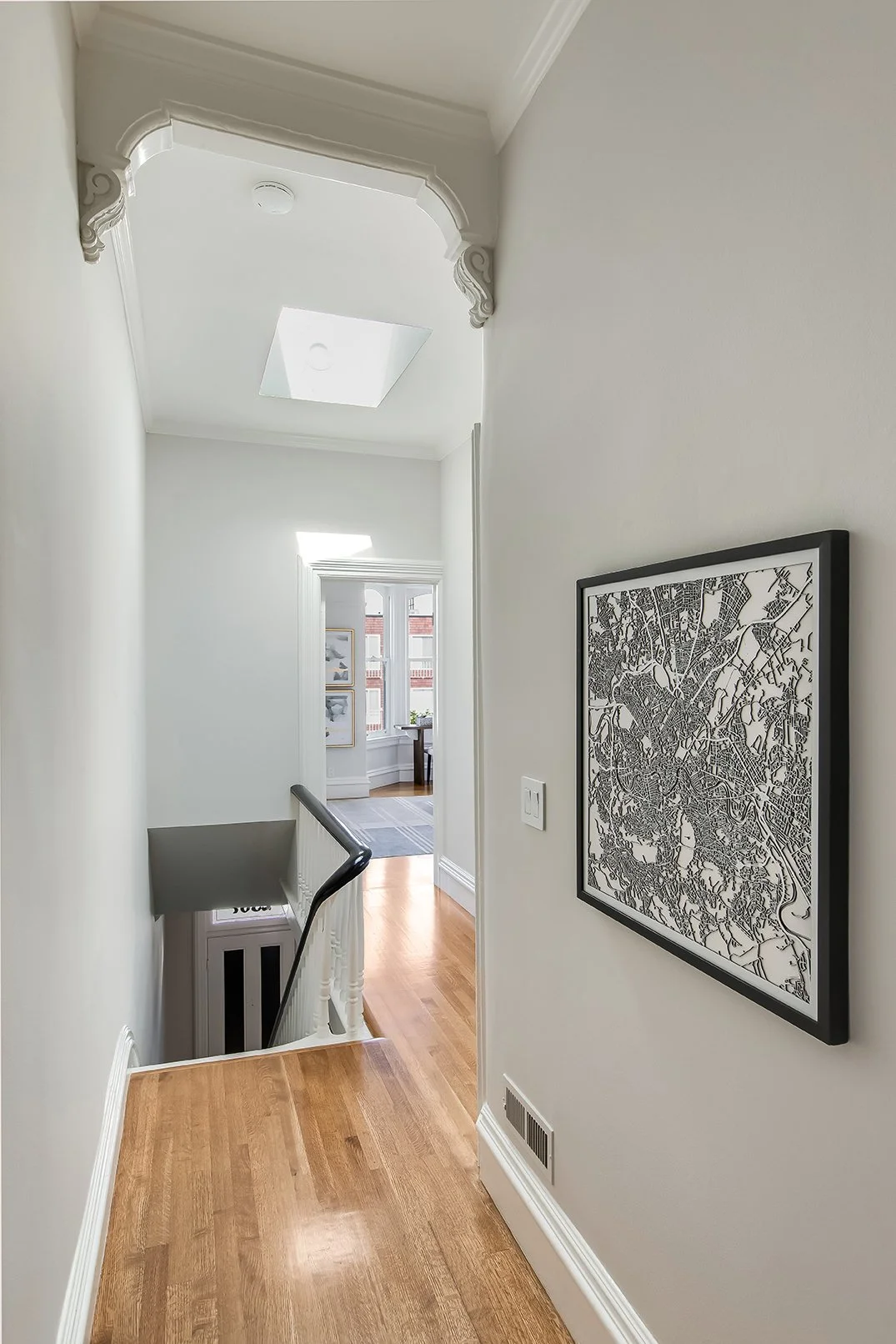 Light-filled upper-level landing with original hardwood floors, a skylight, and decorative Victorian archway details.