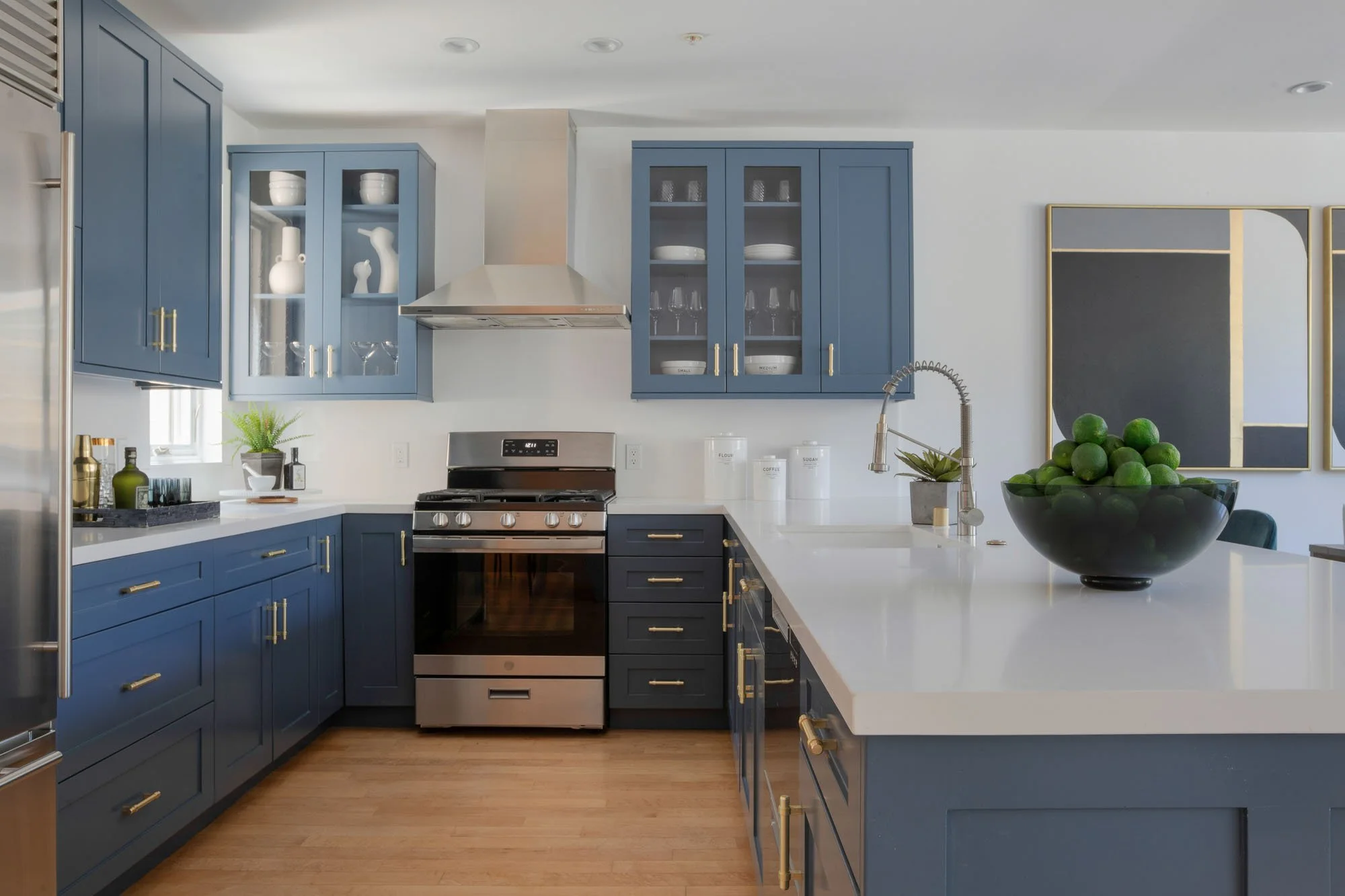 Modern U-shaped kitchen with slate blue cabinetry, gold bar pulls, stainless steel appliances, and a large white quartz island with an undermount sink.