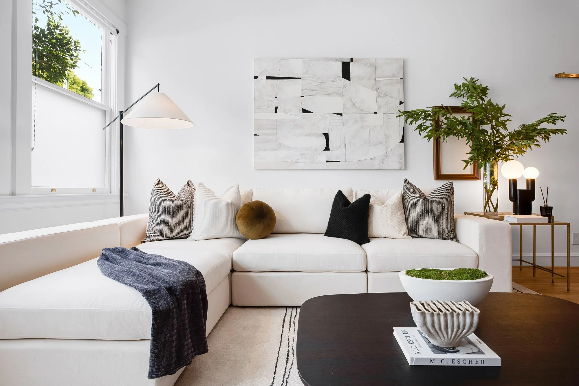 Bright living room in 4545 18th Street San Francisco TIC with cream sectional sofa, large-scale black and white abstract artwork, arc floor lamp, and natural light from double-hung windows