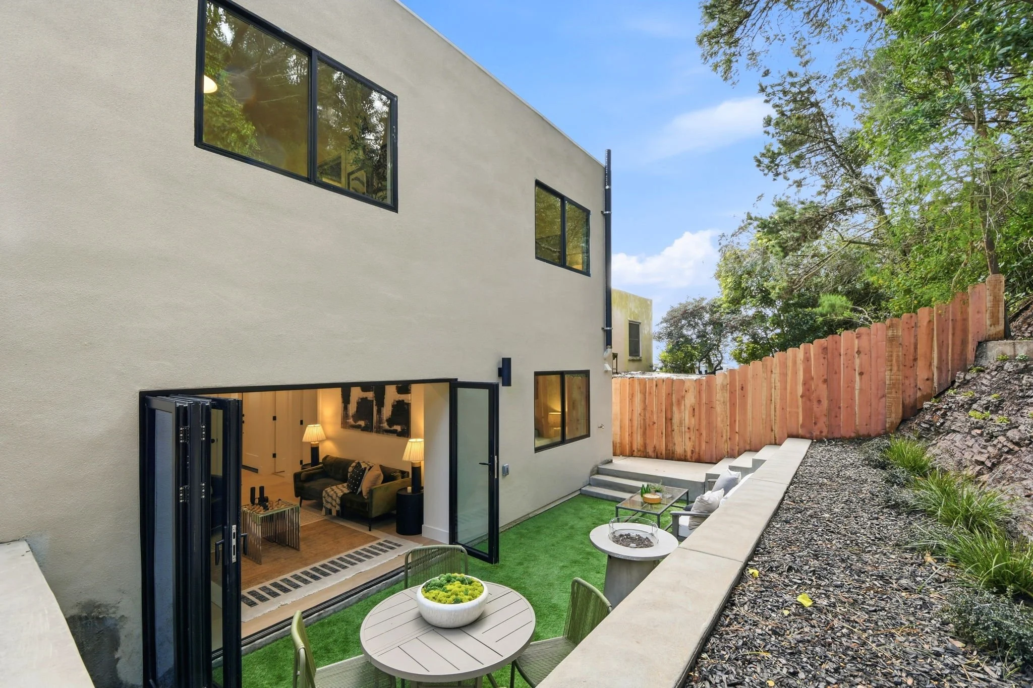 Contemporary patio area with a concrete retaining wall, hillside garden, and bifold glass doors leading into a renovated San Francisco luxury home.