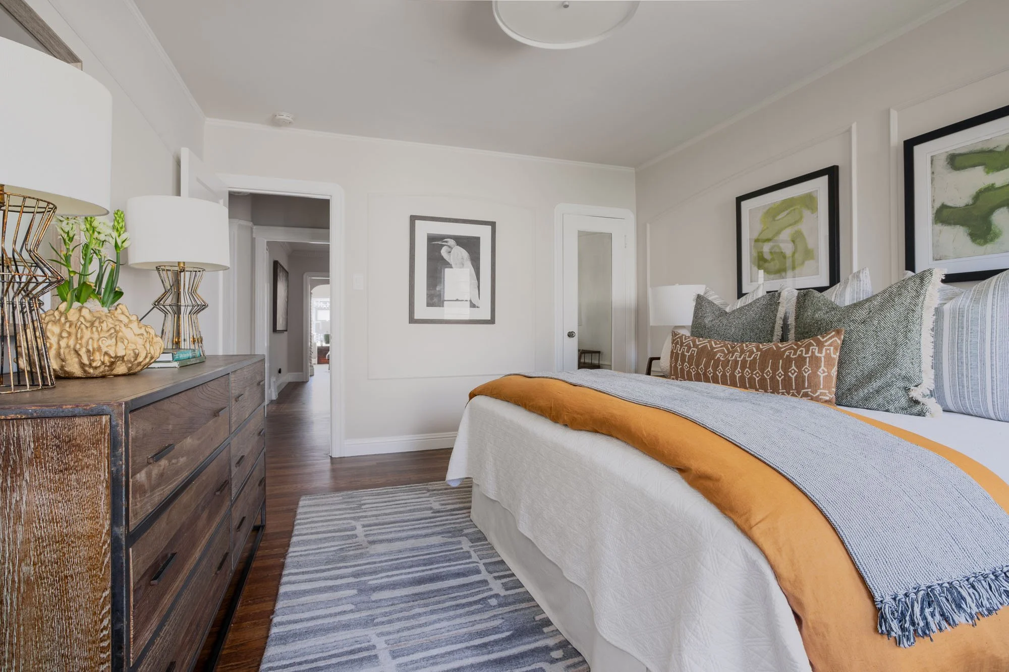 Spacious bedroom interior showcasing a large rustic wood dresser and a clear view into the hallway of this renovated Mission District home.
