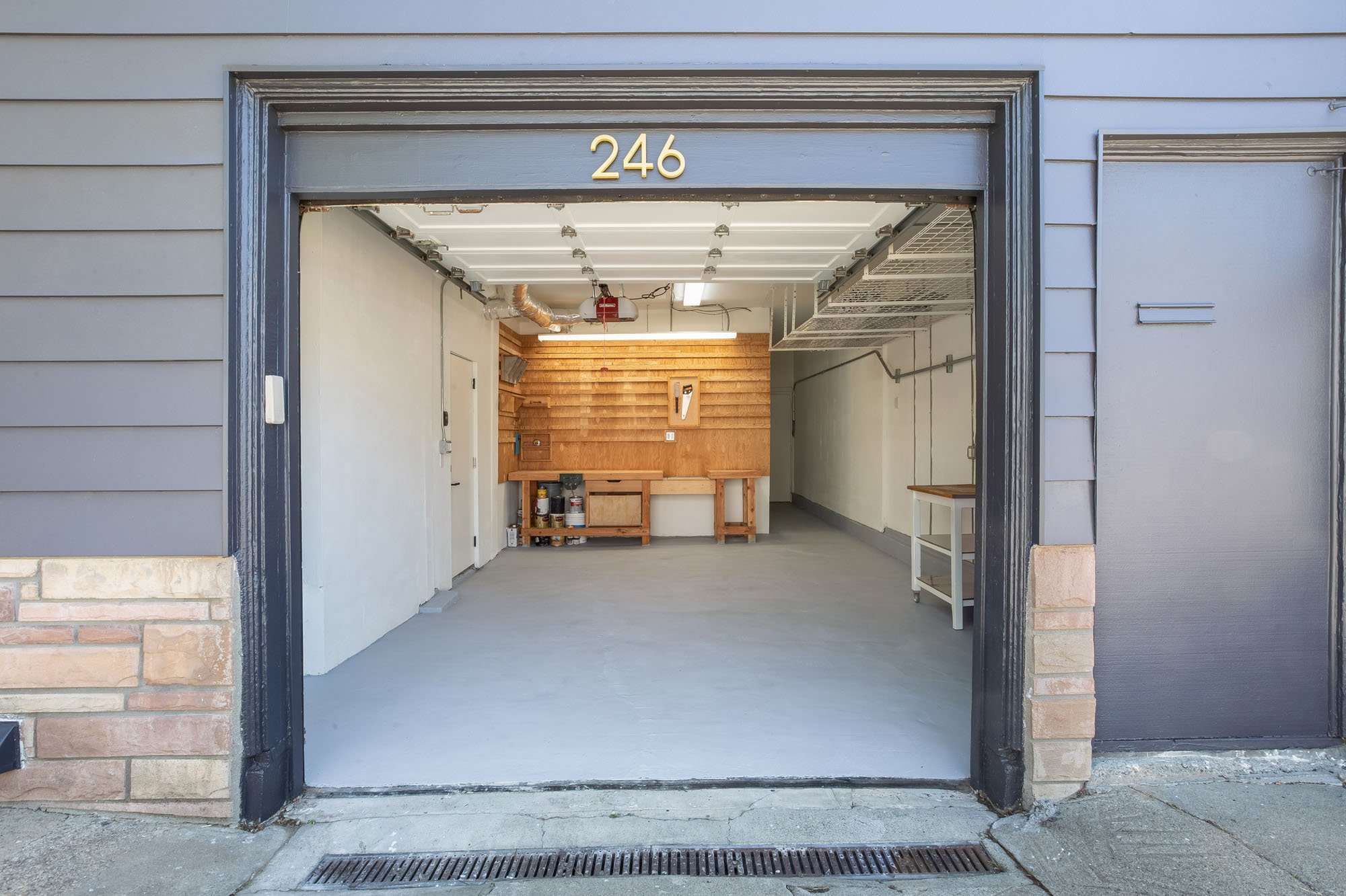 spacious, well-lit garage at 246 Detroit featuring a custom plywood slat-wall workshop, a workbench, and clean gray epoxy floors.