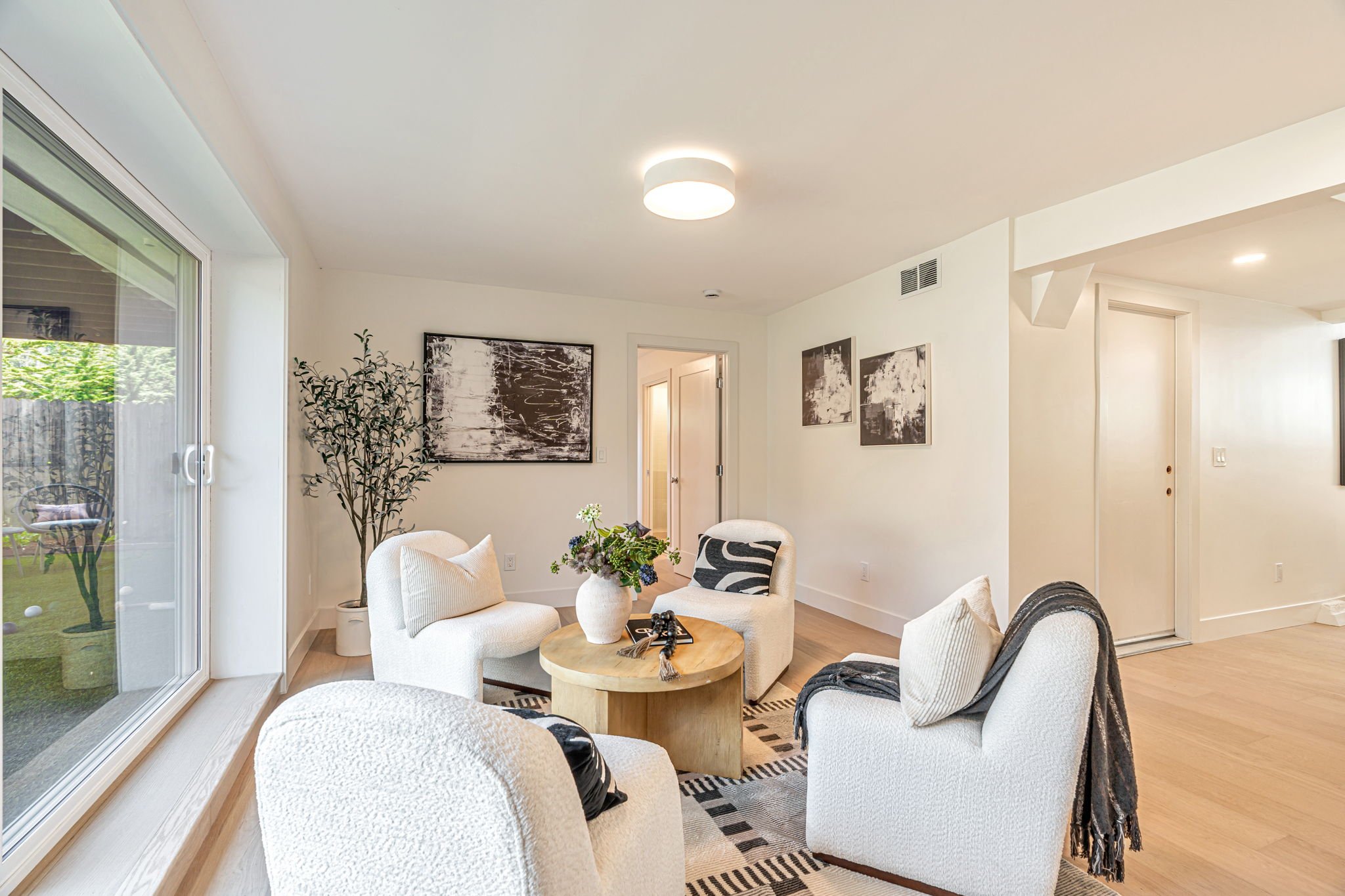 High-end residential lounge area featuring contemporary furniture, abstract art, and a seamless indoor-outdoor flow to a private garden space.