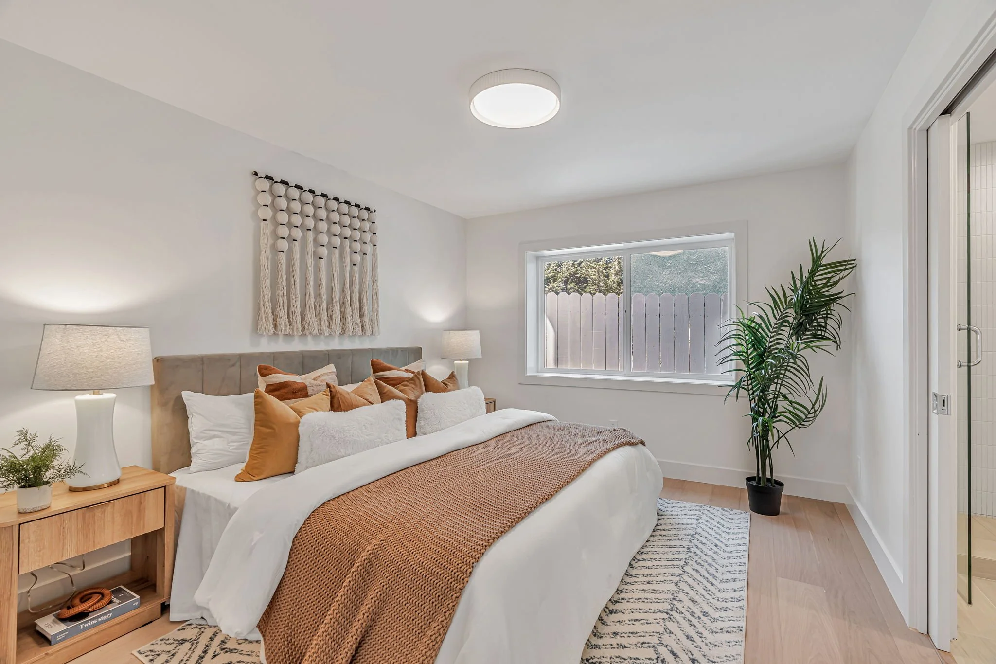 Styled guest suite bed with a velvet headboard, neutral-toned layered bedding, and modern black-and-white accents, optimized for high-end residential staging.