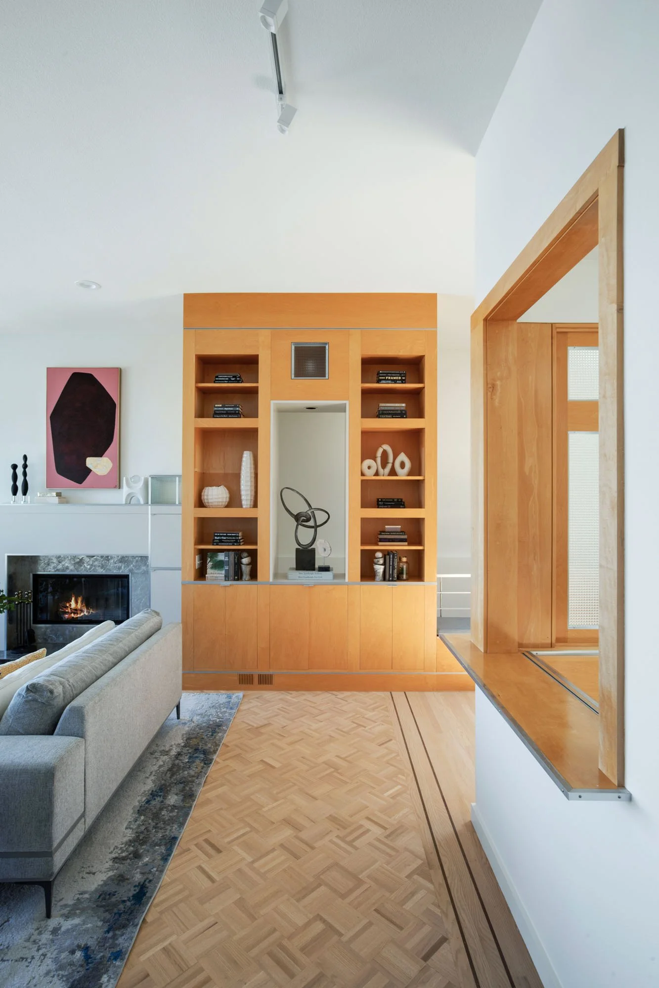 Modern San Francisco living room featuring a custom light-wood built-in entertainment center, parquet hardwood floors, and a sleek grey sofa with an abstract pink and black painting.