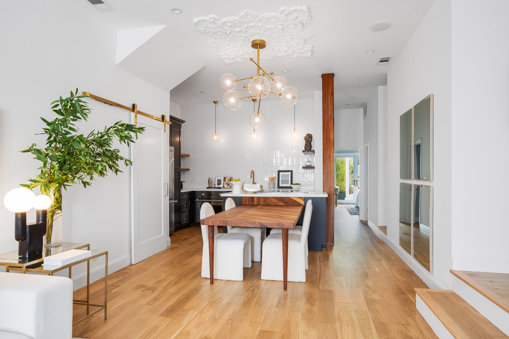 Designer kitchen and dining area in Castro San Francisco TIC with dark navy island, white zellige tile backsplash, gold globe chandelier, ornate plaster ceiling medallion, and walnut live-edge dining table