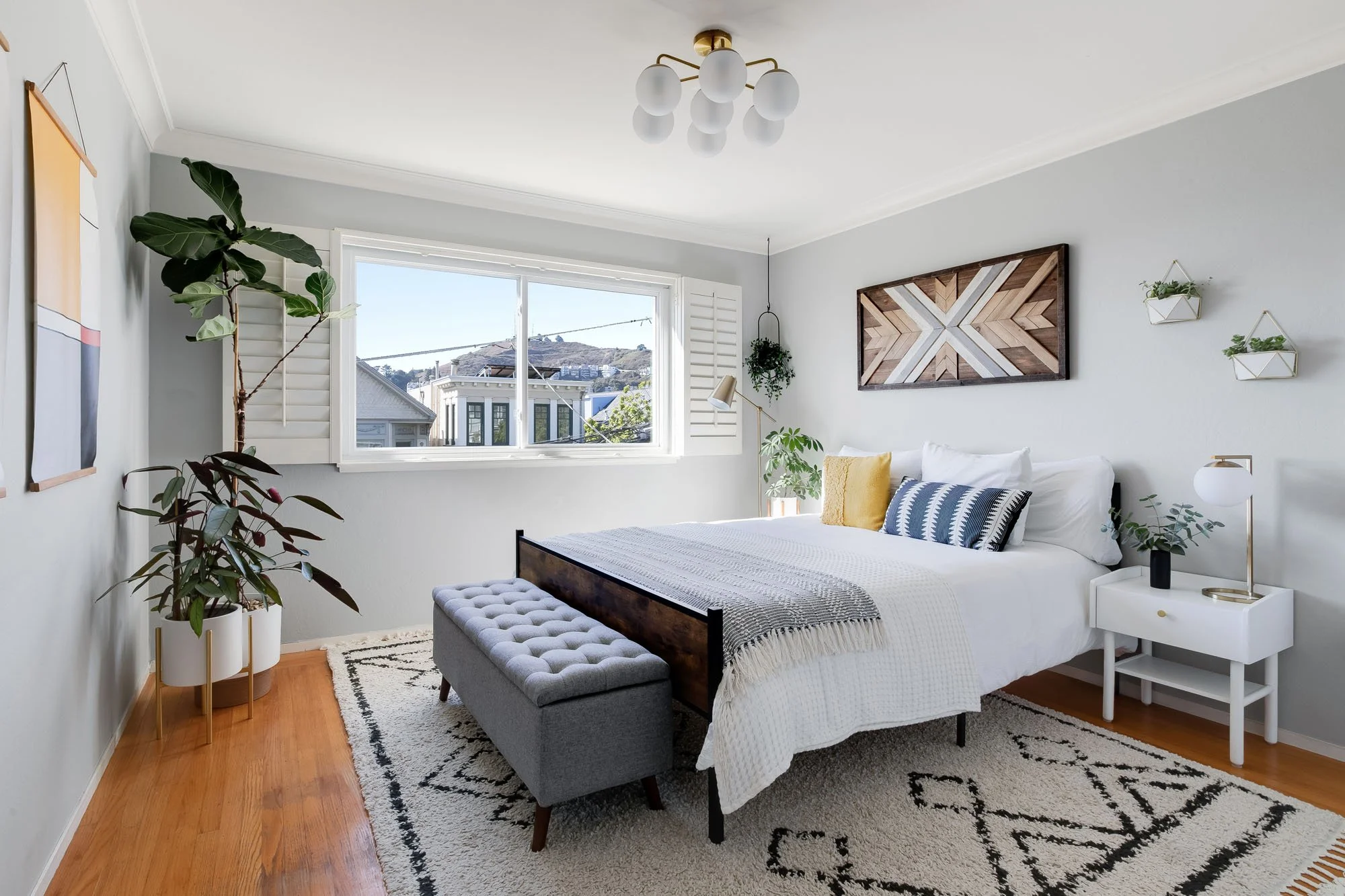 Guest bedroom with a large window overlooking San Francisco hills, featuring a geometric wood wall art piece and a gray tufted bench.