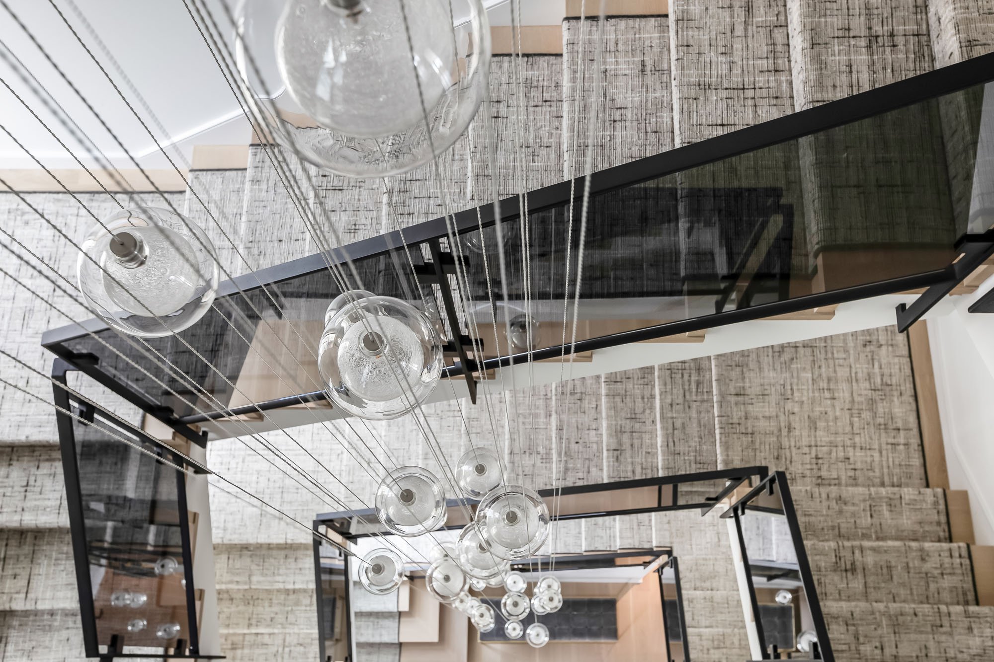 Dramatic top-down view of a modern multi-story staircase at 1647 Sanchez, featuring glass railings and a cascading glass globe chandelier.