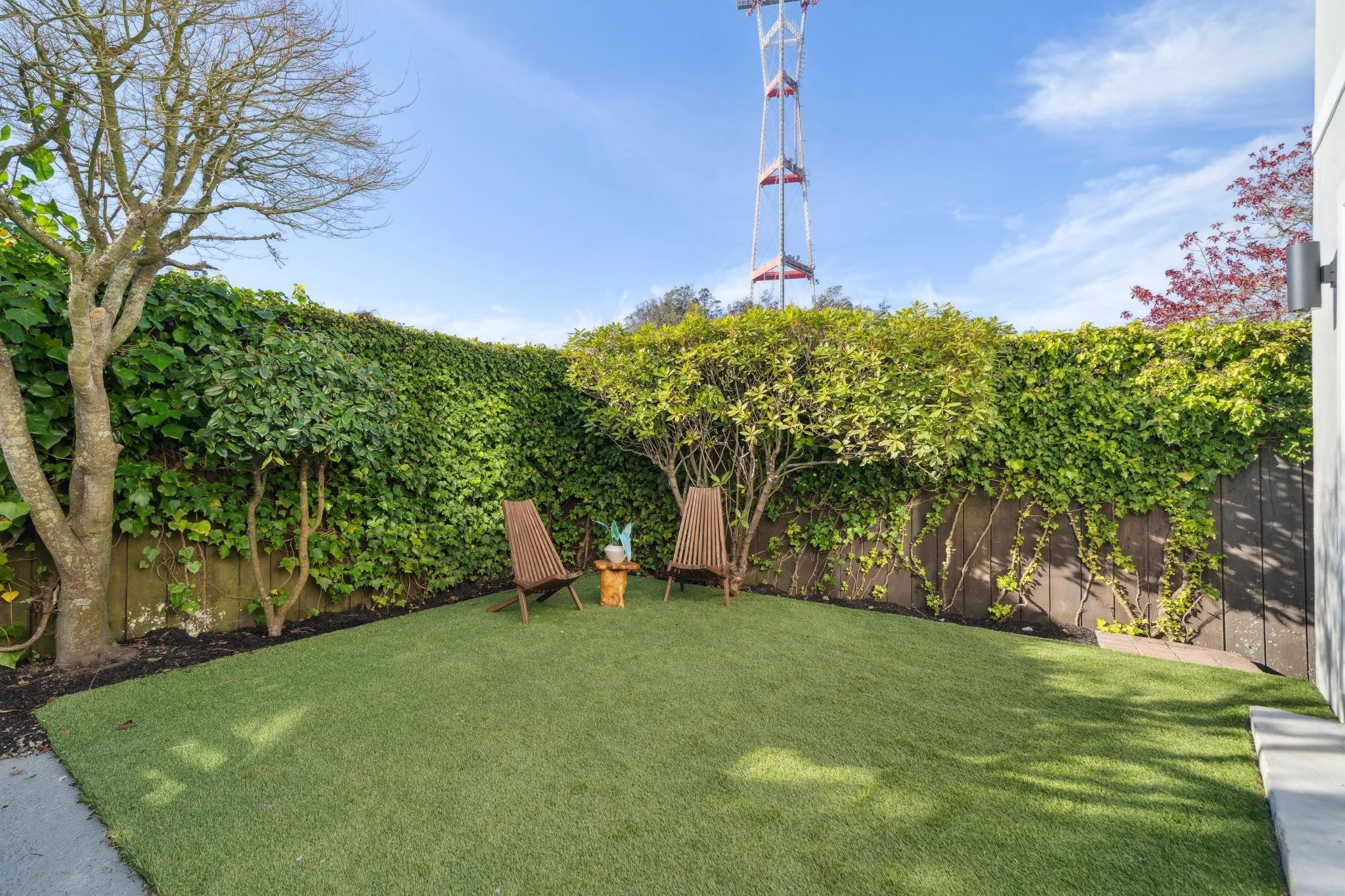 Level backyard with a manicured synthetic grass lawn, lush ivy-covered privacy fence, and two modern wooden lounge chairs.