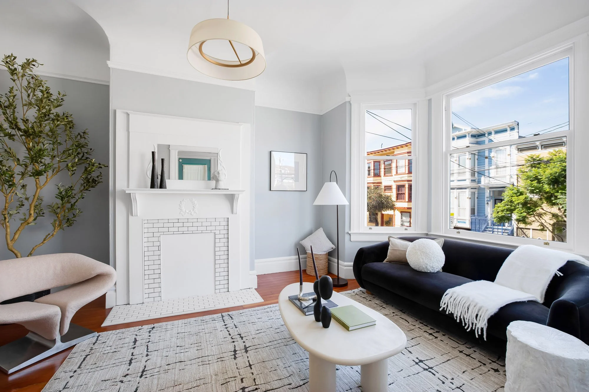 Living room bay window with black sofa, area rug, and a painted fireplace mantel with white subway tile surround