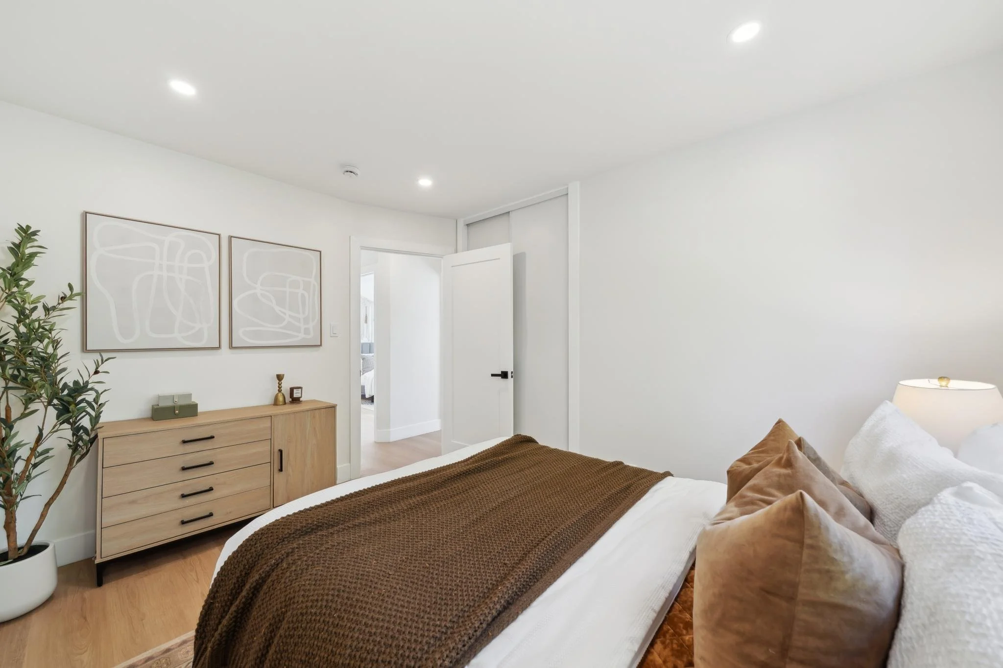 View from the bed toward a light wood dresser and abstract wall art, showing the clean lines and contemporary design of the renovated guest wing.