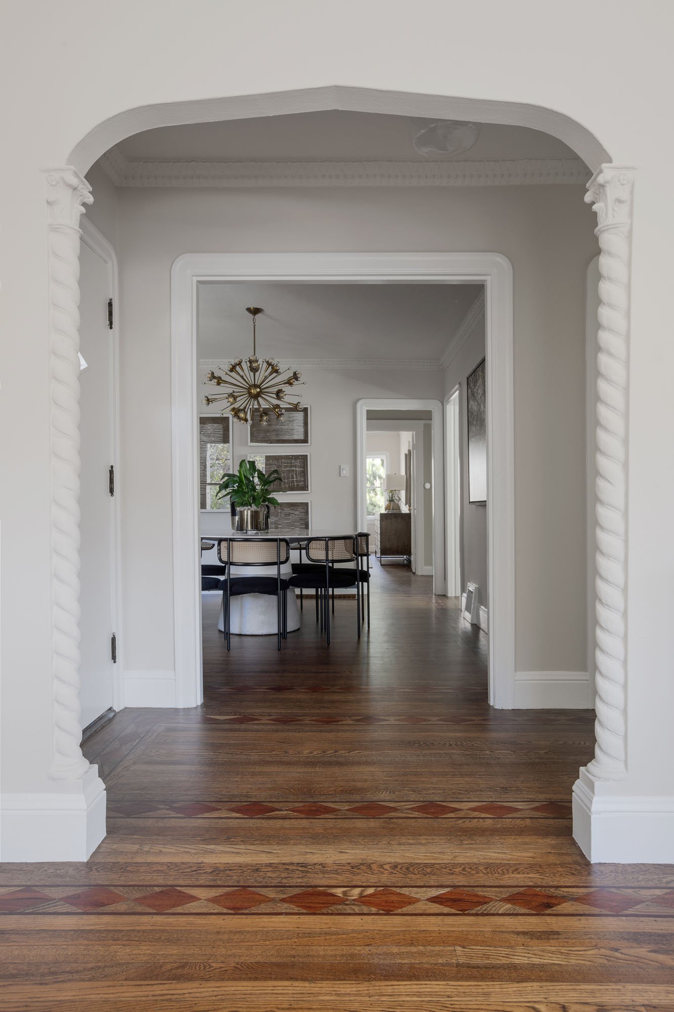 Elegant interior perspective through barley-twist columns leading to a formal dining room with a mid-century starburst chandelier.