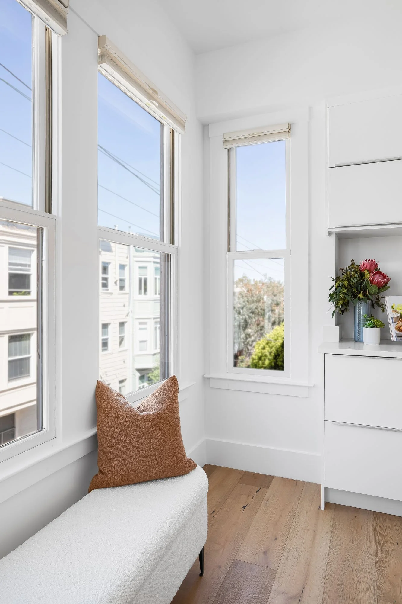 Sunny window seating area in a Mission Dolores condo featuring a white bouclé bench and rust-colored accent pillow.