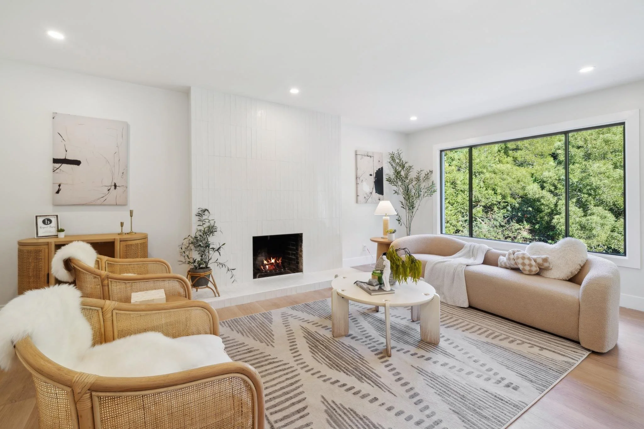 Modern living room interior featuring a white tiled fireplace, rattan lounge chairs with sheepskin throws, and a large window overlooking lush greenery in San Francisco.