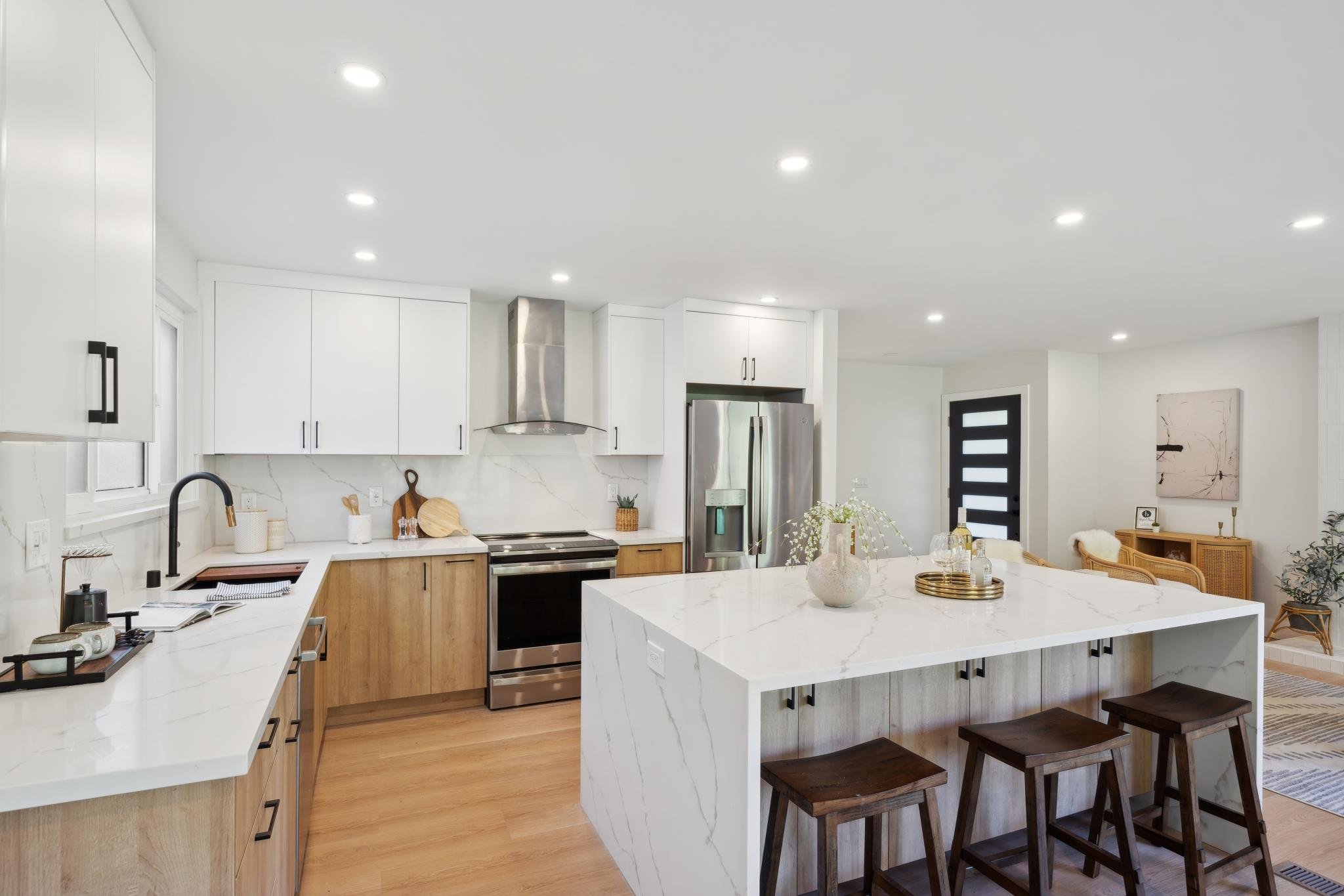 Wide-angle view of a renovated kitchen and living space, highlighting the natural light, marble surfaces, and modern Scandinavian design elements.