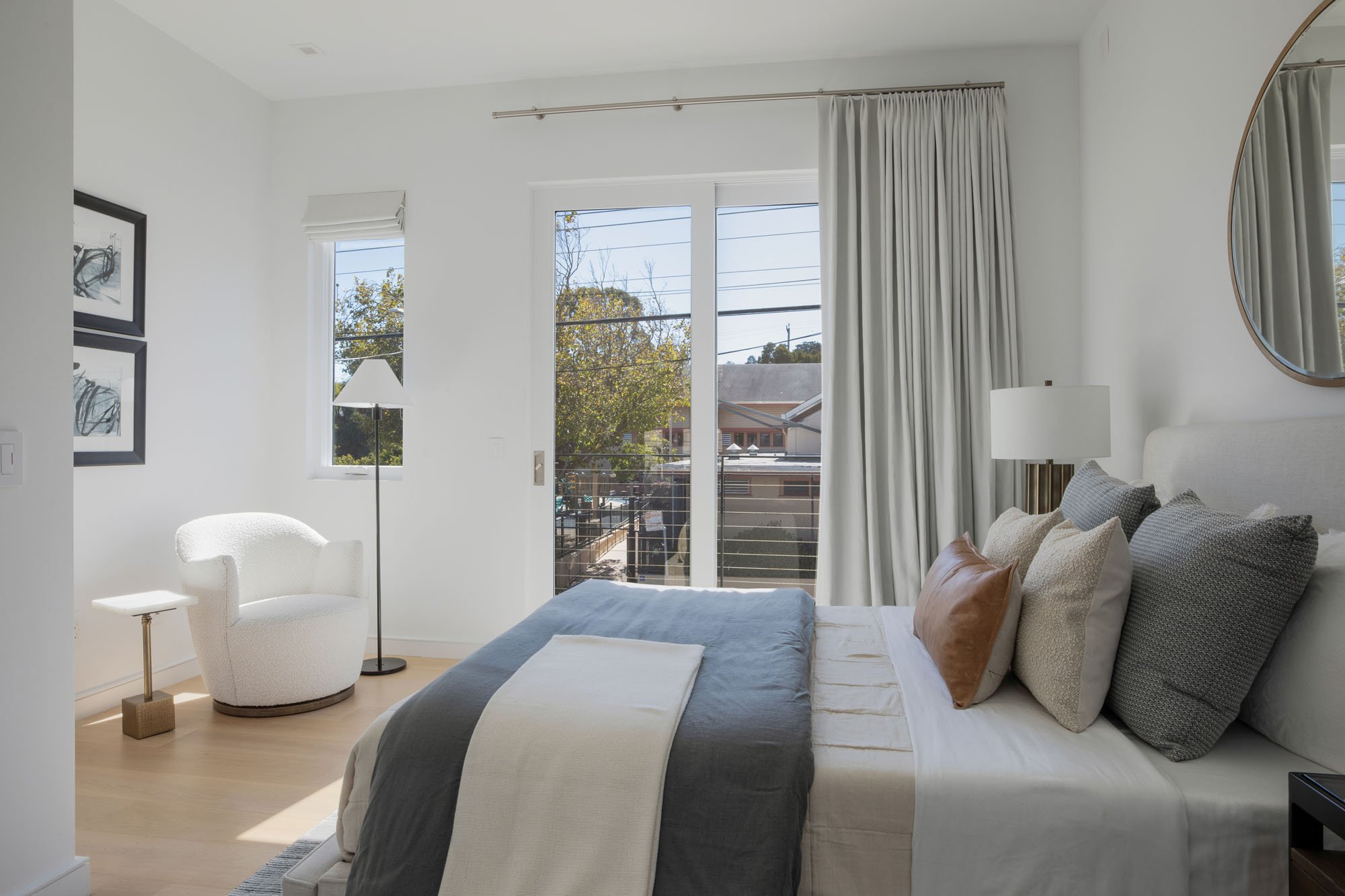 Elegant guest bedroom at 290 Day St featuring a white boucle swivel chair, designer neutral bedding, and a private balcony overlooking the city