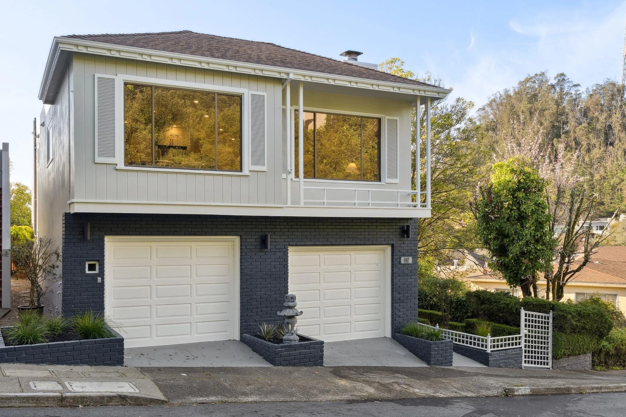 Street-level view of 147 Gladeview Way featuring a clean mid-century modern exterior, white siding, dark grey brick garage level, and large windows reflecting the surrounding trees.